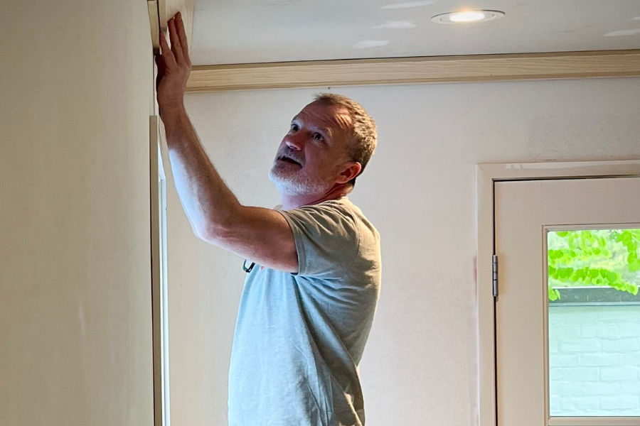 An older man inspecting or working on the ceiling near a door, inside a house.