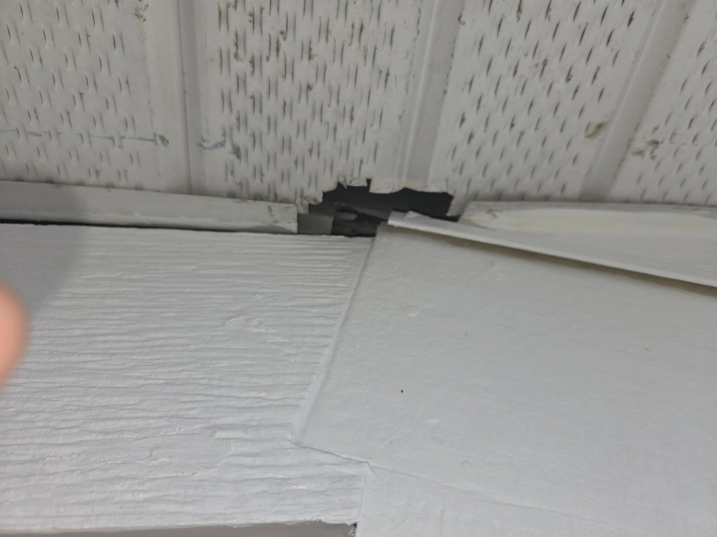 Close-up of ceiling and wall corner with visible damage including a hole and broken drywall, revealing insulation and internal structure.