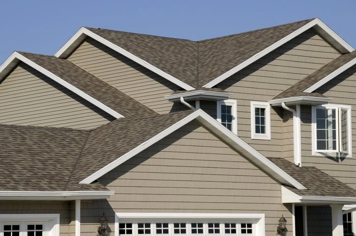 Close-up of the roof and upper part of a beige house with multiple gables, white trim, and small windows.