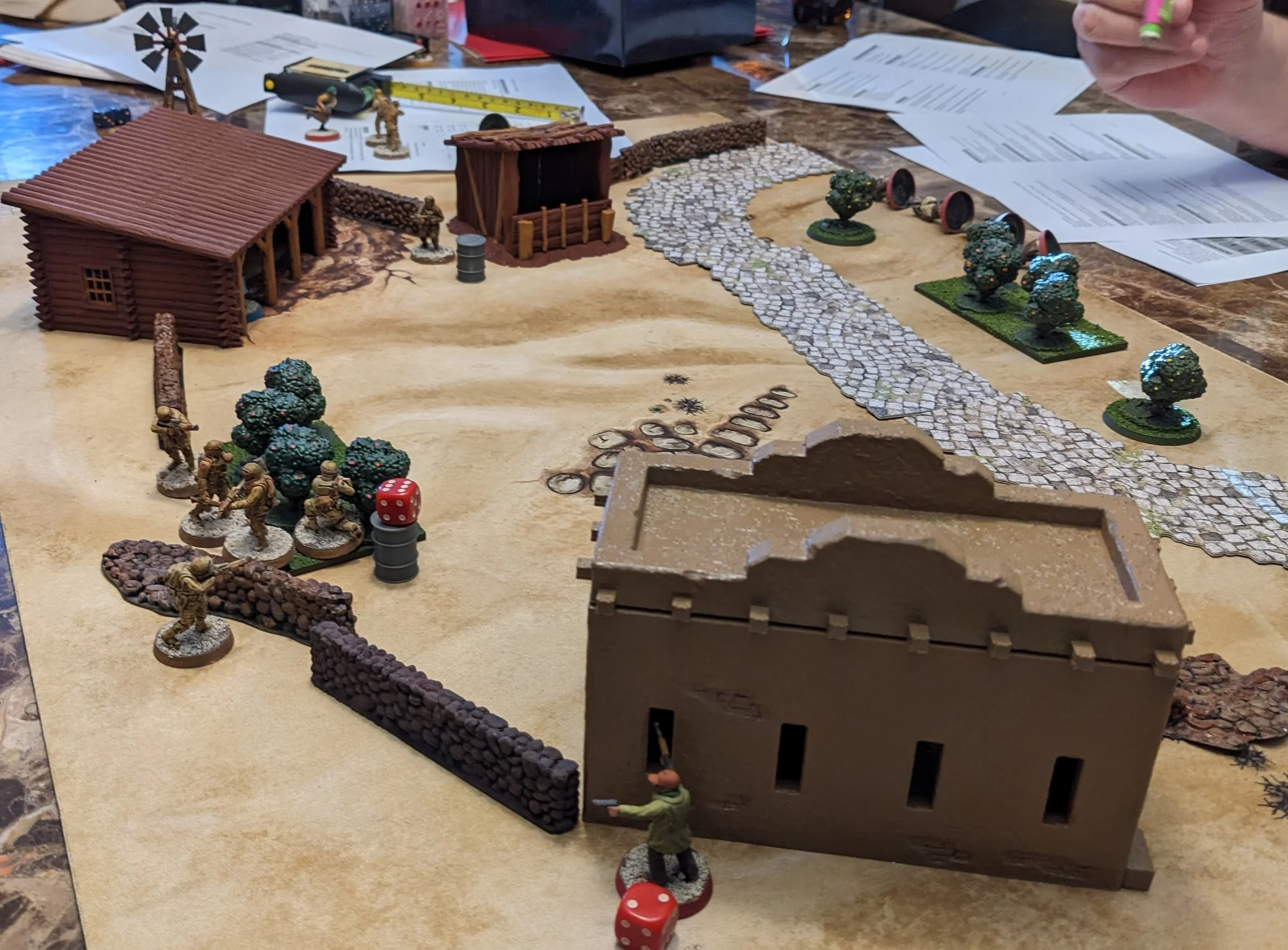 Tabletop game setup with miniatures, buildings, and terrain, resembling a World War II scene.