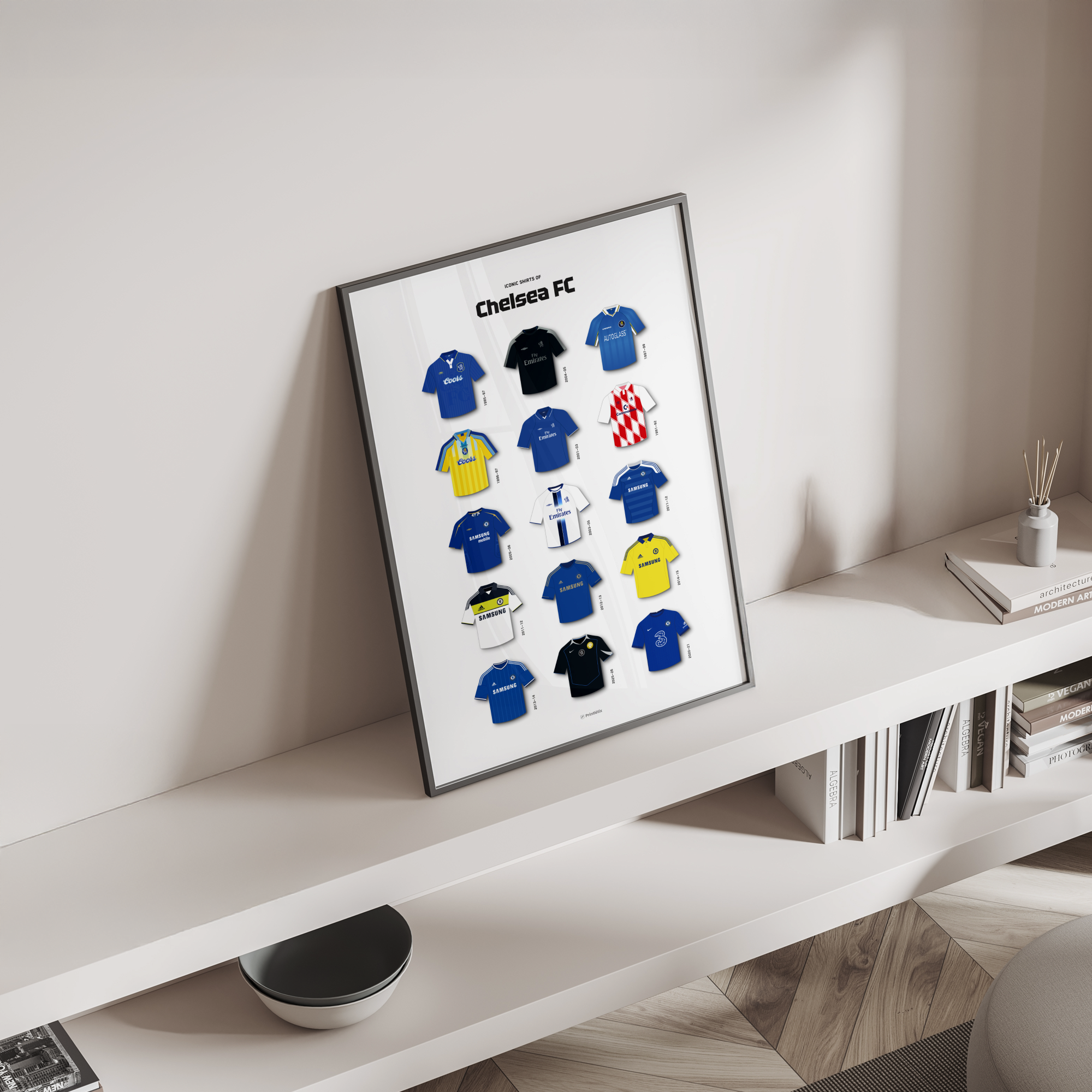 Framed Chelsea football kit evolution poster leaning on a modern white shelf with books and decor.