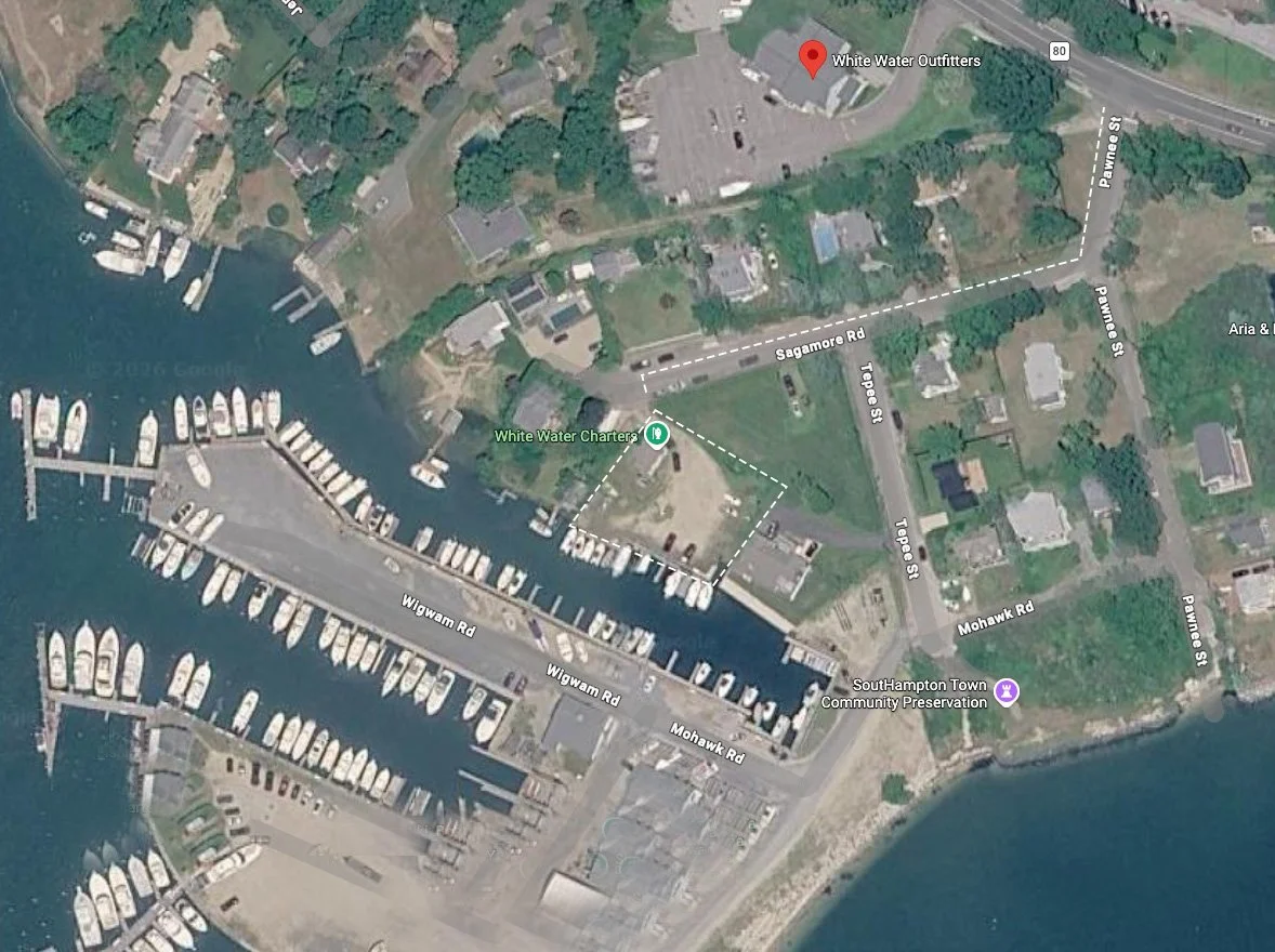 Aerial view of a marina with boats docked along piers, surrounded by roads and residential areas. There are marked paths and labels, including White Water Charter, Southhampton Town Community Preservation, and street names.