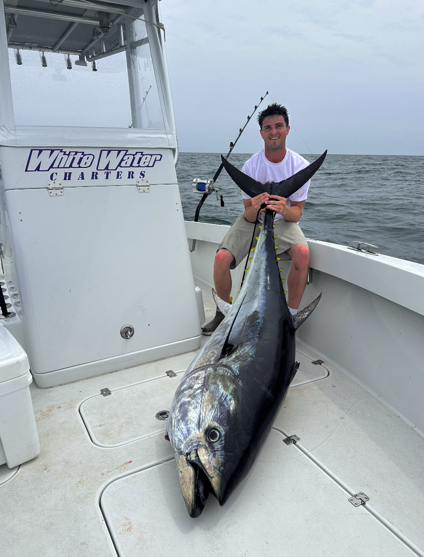 Man sitting on a boat holding a large tuna fish he caught.