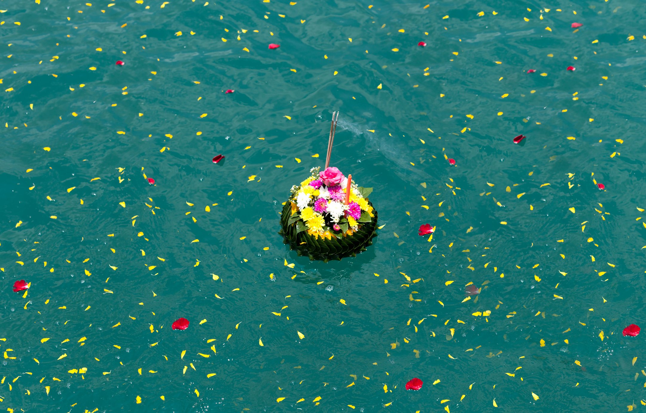 A floating floral arrangement with pink, yellow, and white flowers on water, surrounded by scattered red and yellow flower petals in the Hamptons during a fishing charter
