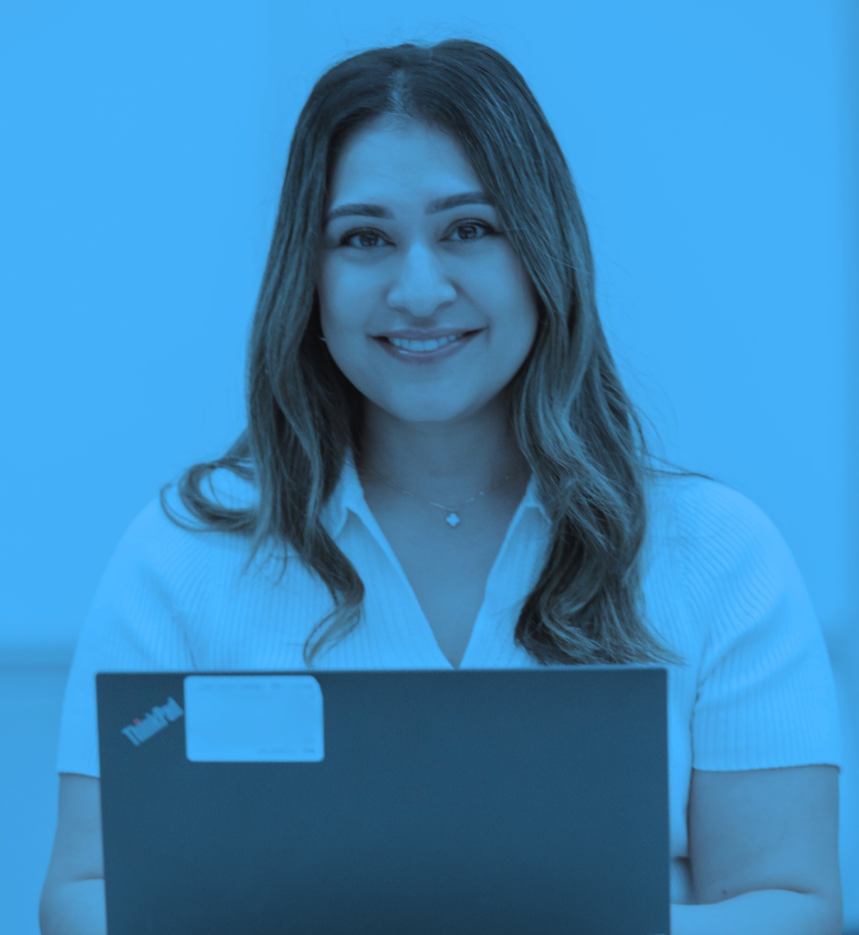 A woman with long brown hair smiling, holding a closed laptop, wearing a white shirt and a necklace against a blue background.