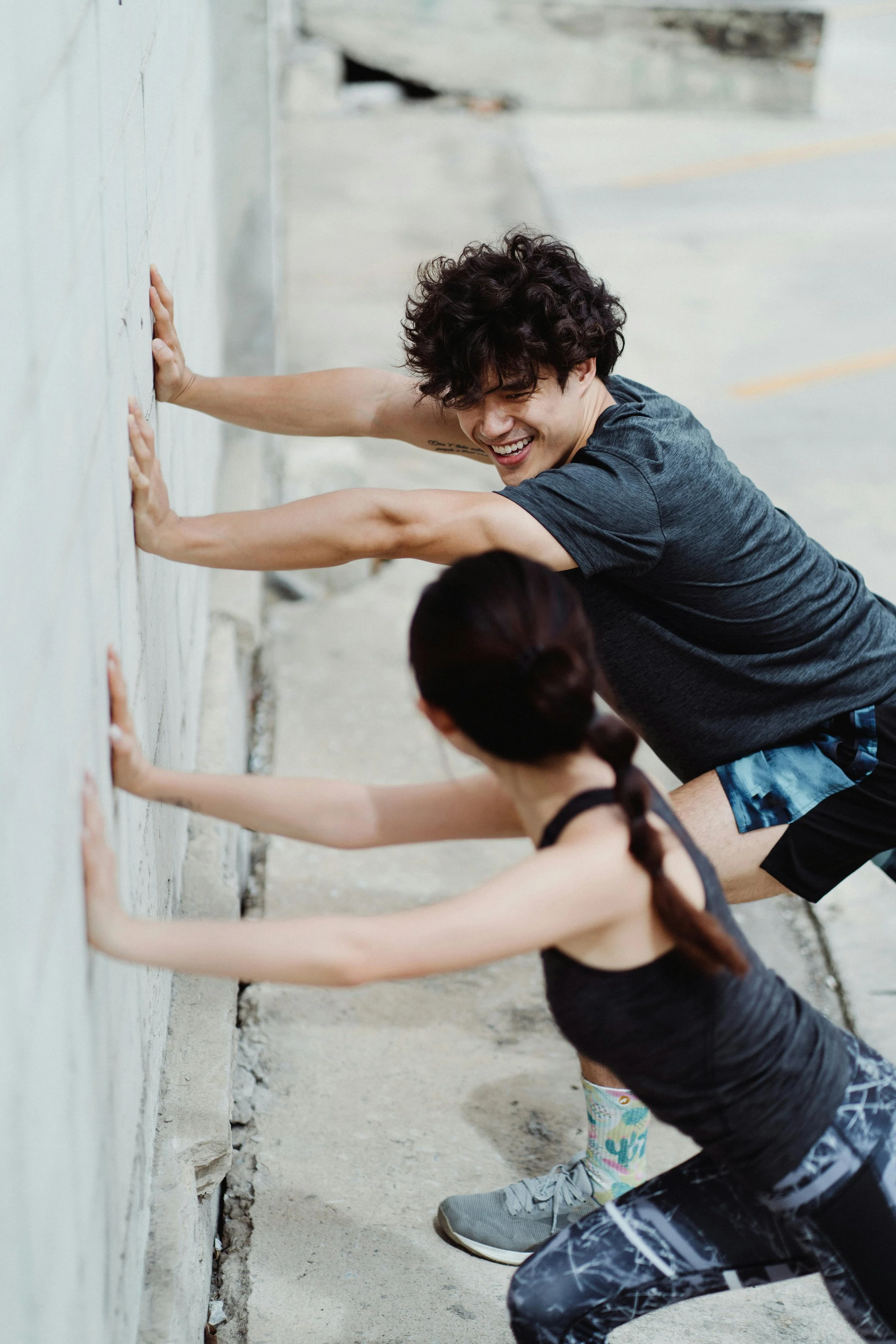 Deux personnes, un homme et une femme, faisant de l'escalade contre un mur extérieur, souriant et s'encourageant.