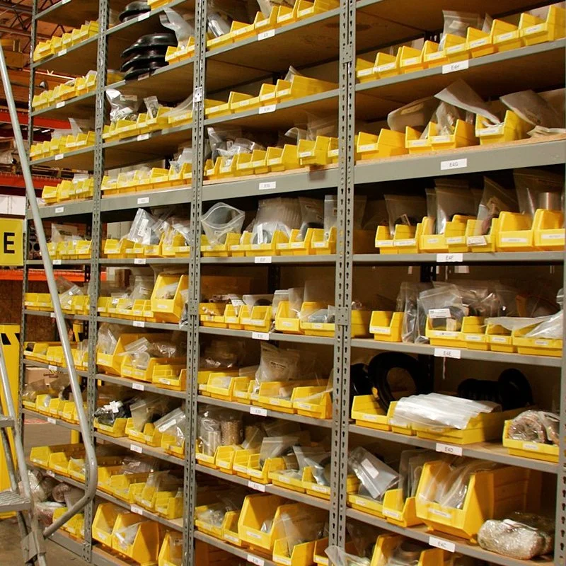 Factory shelves stocked with various mechanical parts in yellow trays, organized for industrial assembly or maintenance.