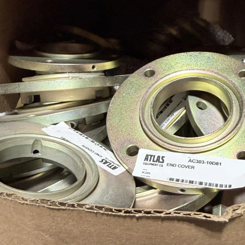 A box filled with metal end covers or flanges, some with labels indicating model number and manufacturer, used in machinery or equipment assembly.