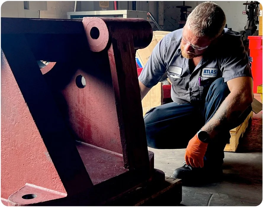 A man working on a large red industrial metal component, kneeling down in a workshop.