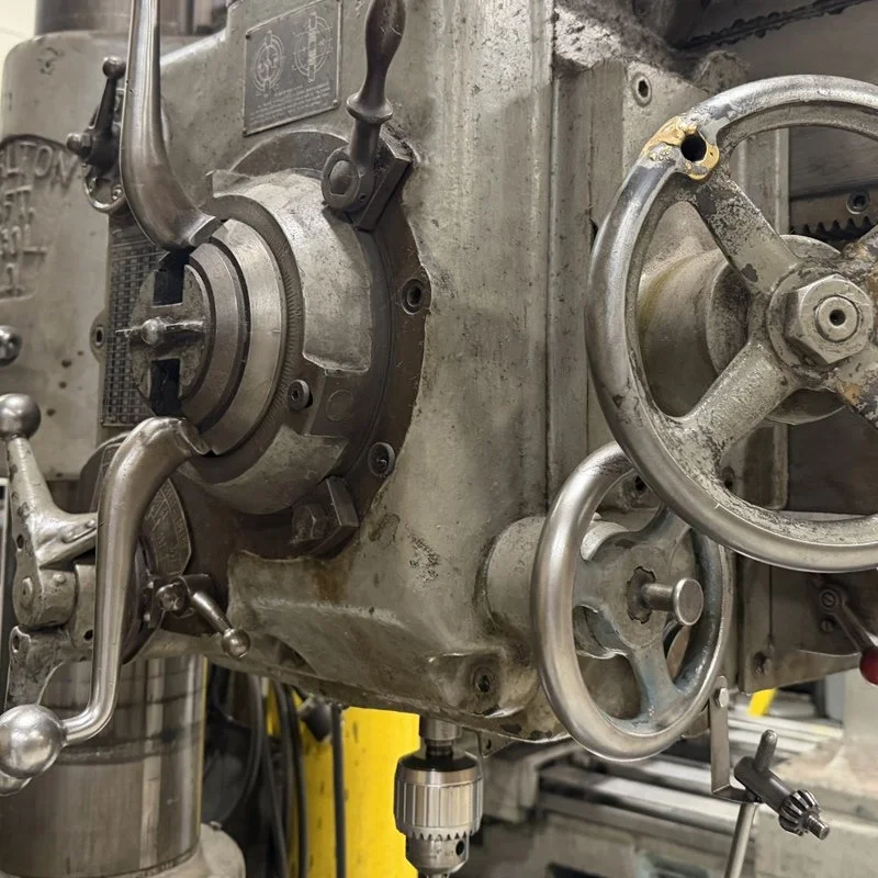 Close-up of a vintage metal lathe machine with various handwheels and controls.