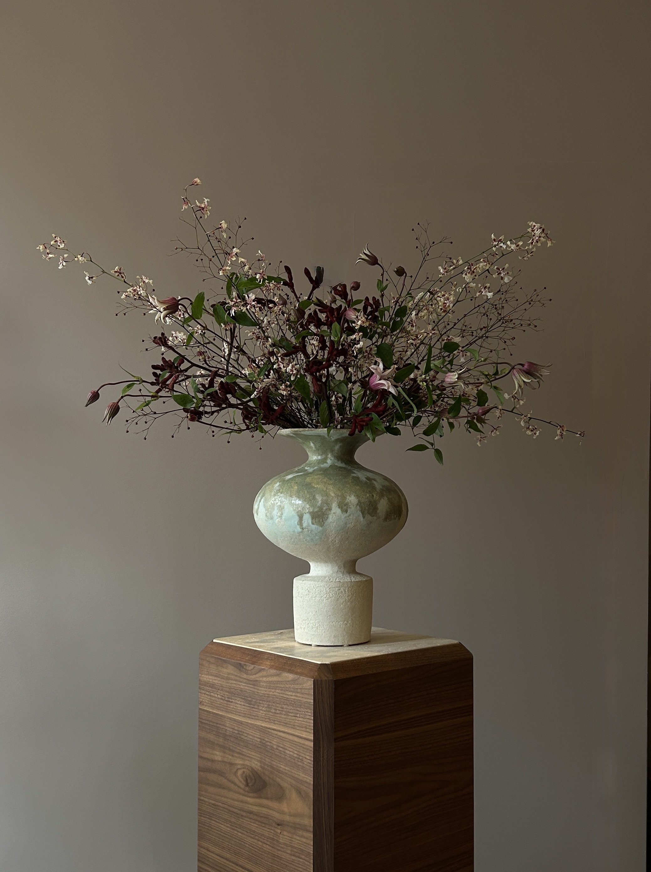 A decorative flower arrangement in a ceramic vase on a wooden pedestal.