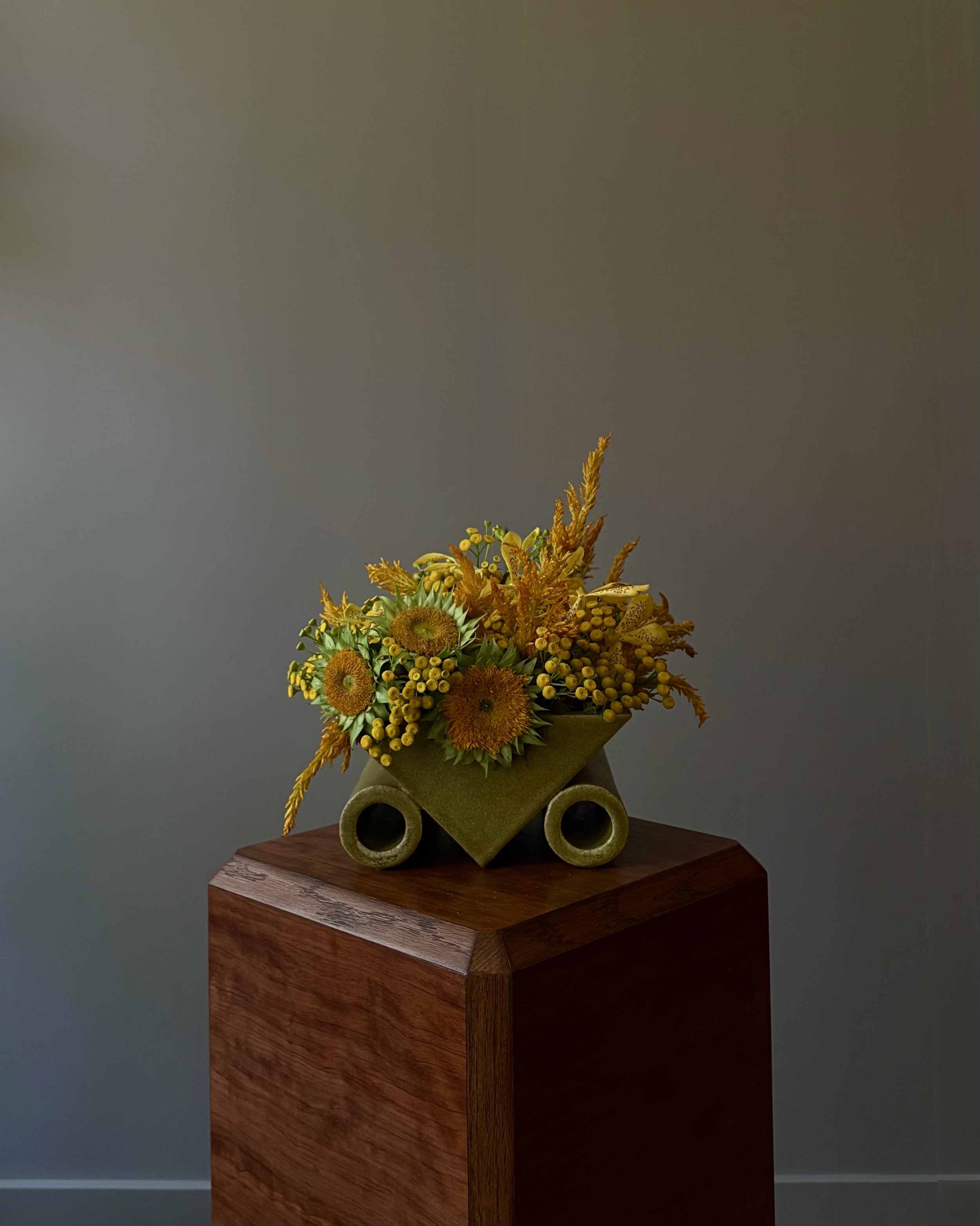 Yellow and orange flower arrangement in a green vase on a wooden stand