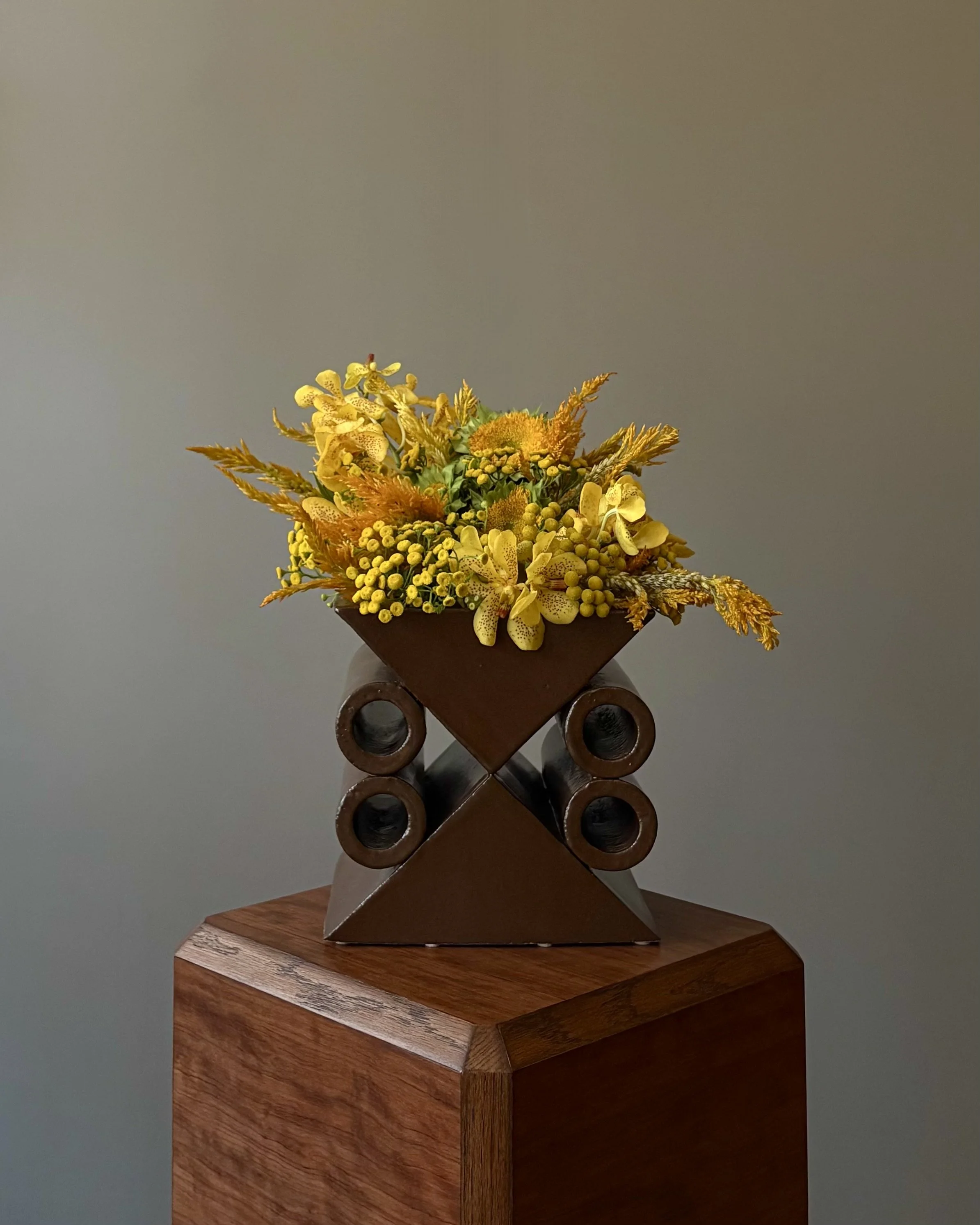 Yellow floral arrangement on a modern metal sculpture displayed on a wooden pedestal.