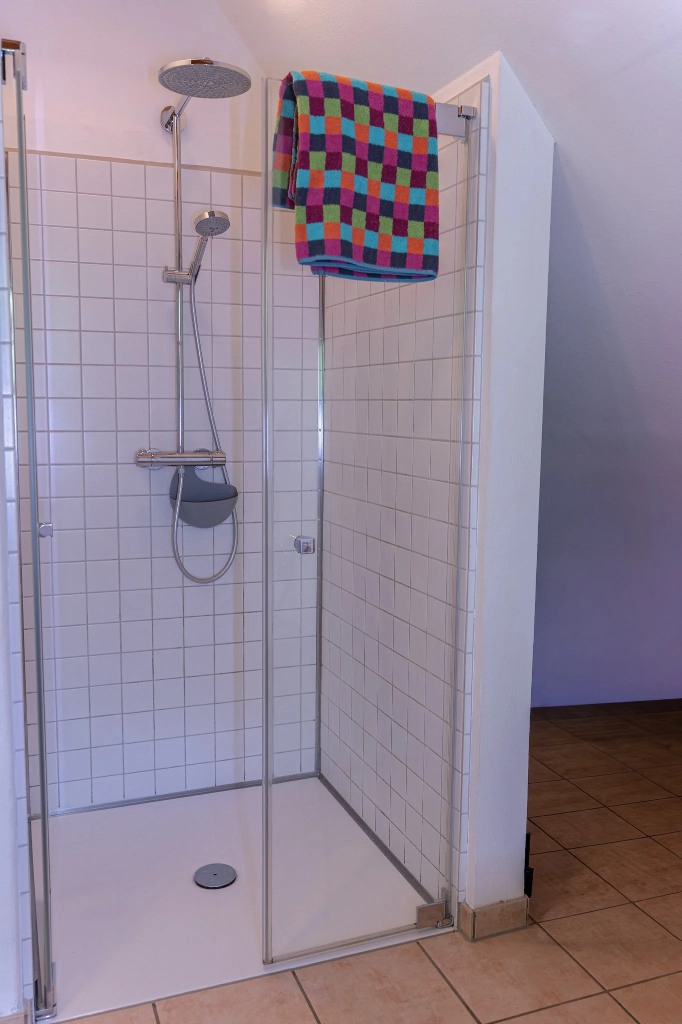 Duschkabine mit zwei Duschköpfen, einer Handbrause, buntem Handtuch und weißen Fliesen