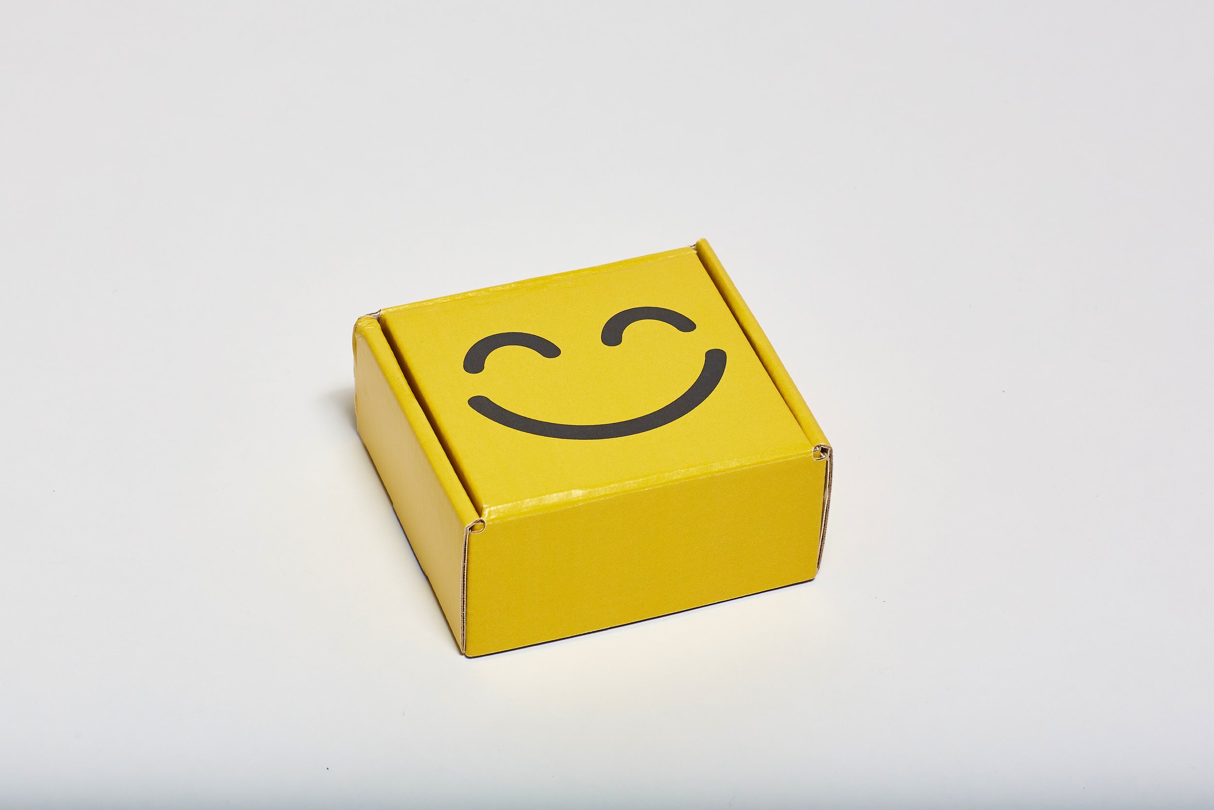 Yellow cardboard box with a smiling face with closed eyes printed on its top.