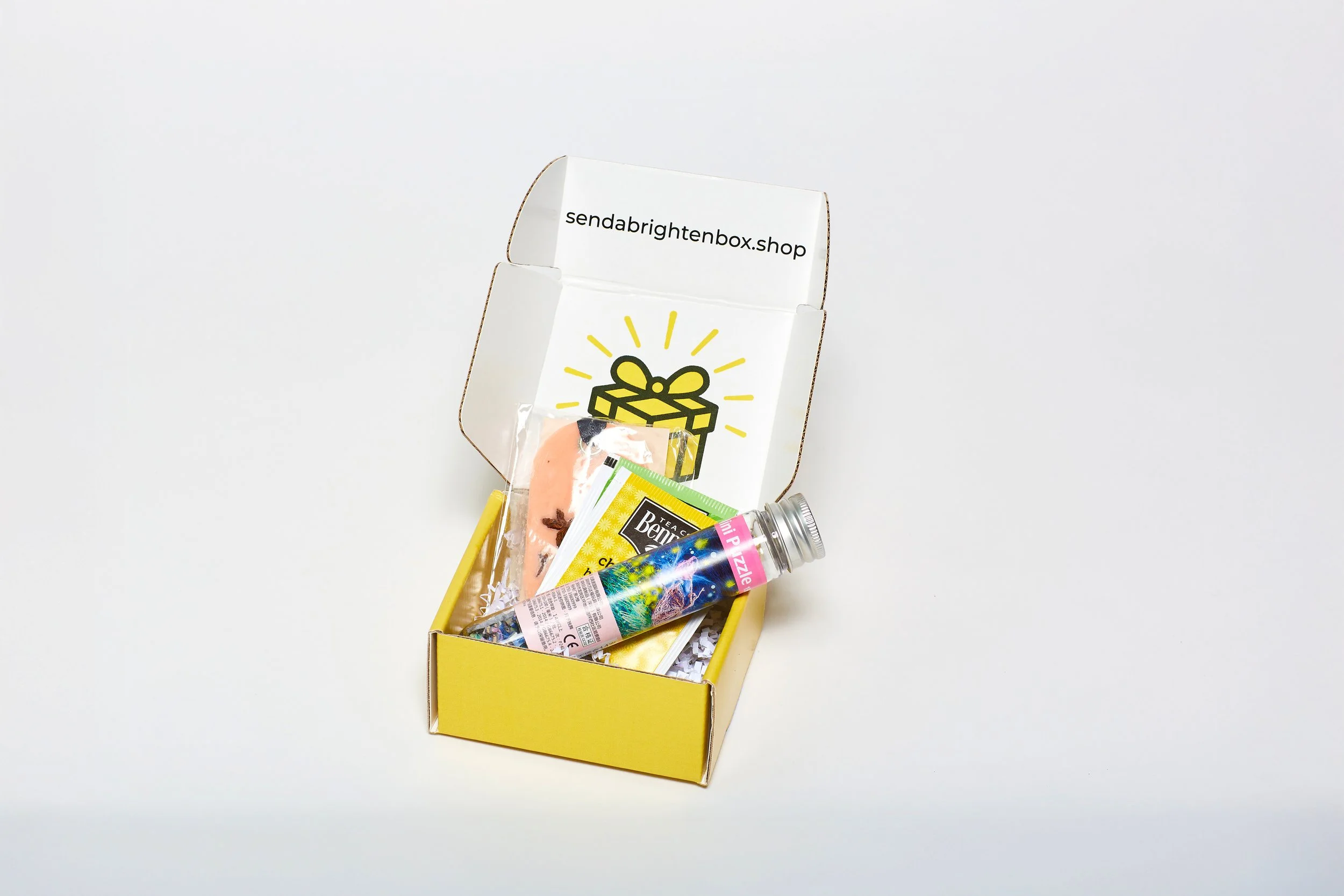 Open yellow and white gift box with party supplies and small gifts inside, on a white background.