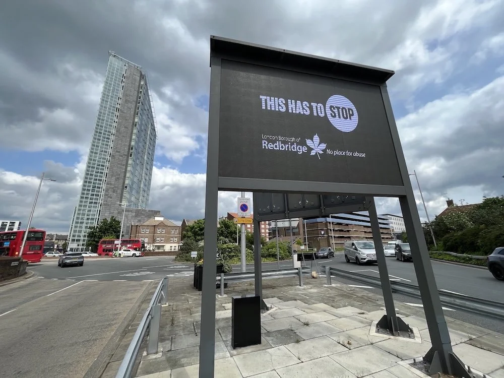 A street banner that says 'THIS HAS TO STOP,' with the London Borough of Redbridge logo, saying 'no place for abuse' next to the logo.