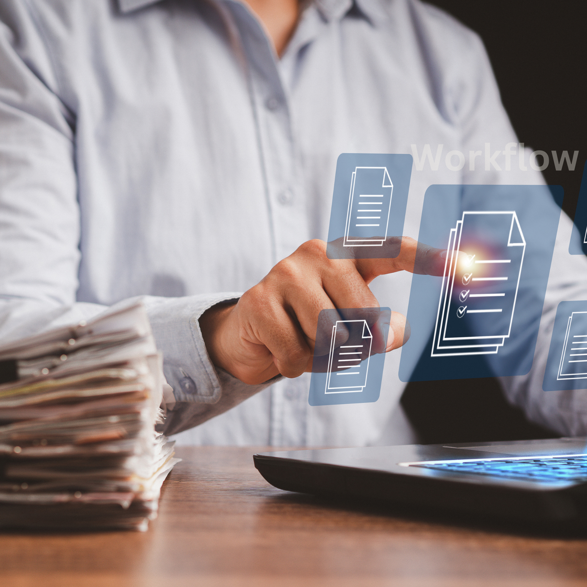 Person in a gray shirt interacting with digital icons of documents on a futuristic touchscreen interface over a computer keyboard, with a large stack of papers on the left.