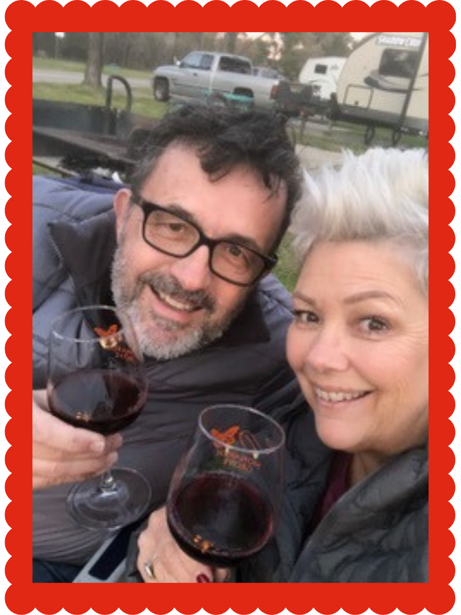 A smiling man with glasses and a beard holding a glass of red wine with his wife
