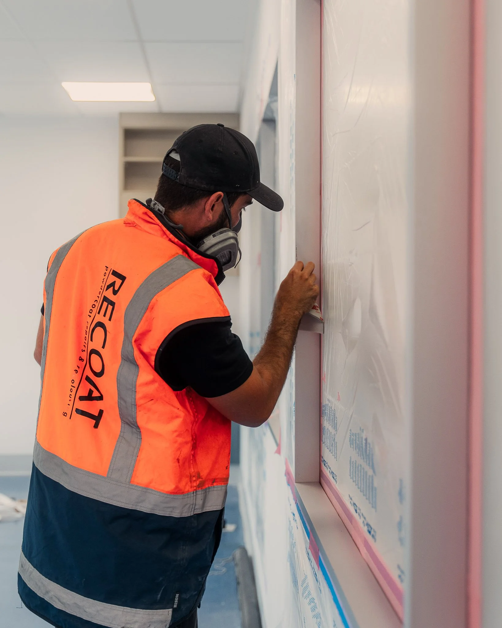 A construction worker wearing an orange safety vest and a black cap, cleaning a whiteboard with a cloth in a building under construction.