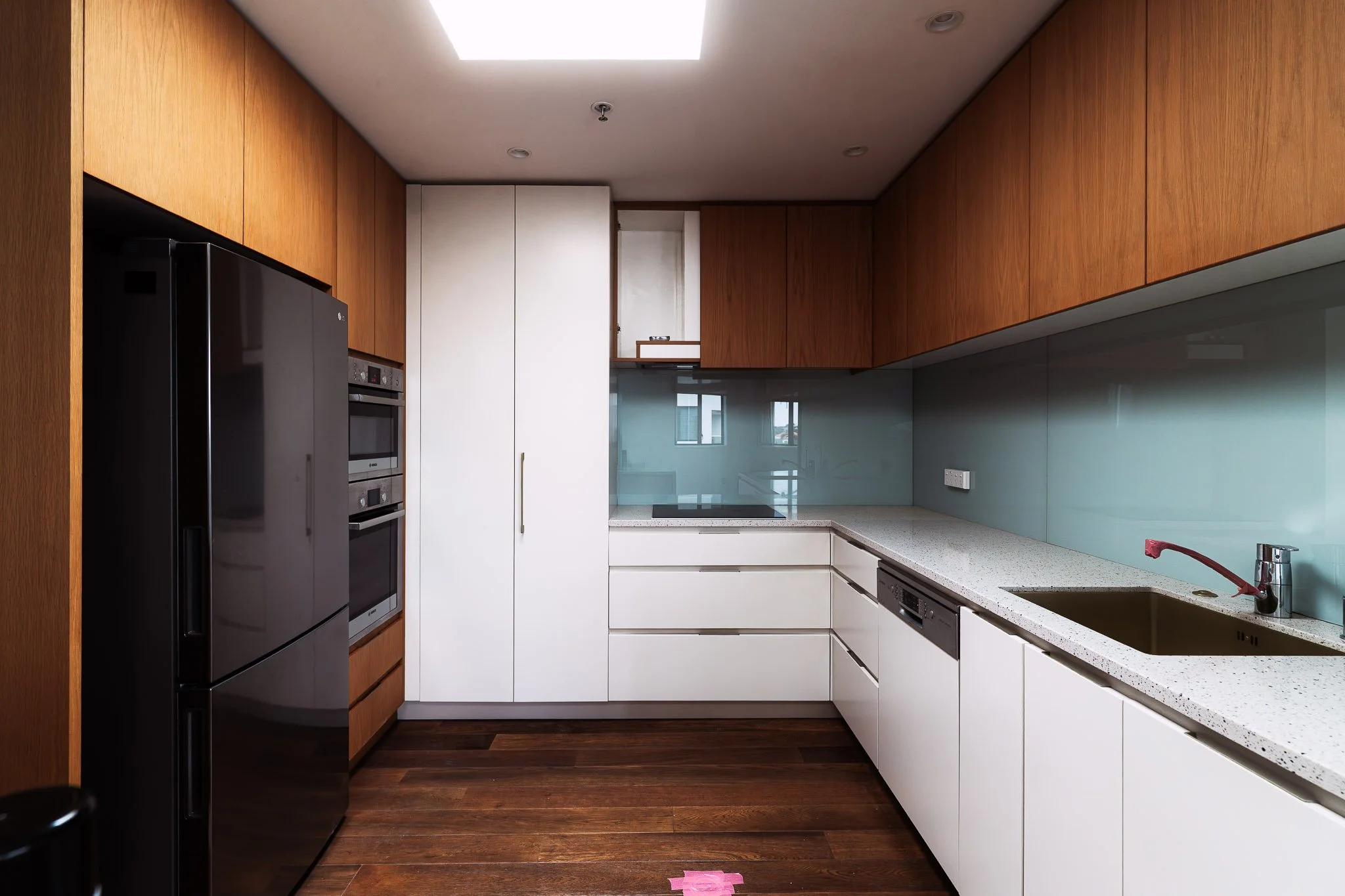 Modern kitchen with white cabinets, wooden upper cabinets, a black refrigerator, a built-in oven, and a speckled white countertop with an undermount sink and modern faucet.