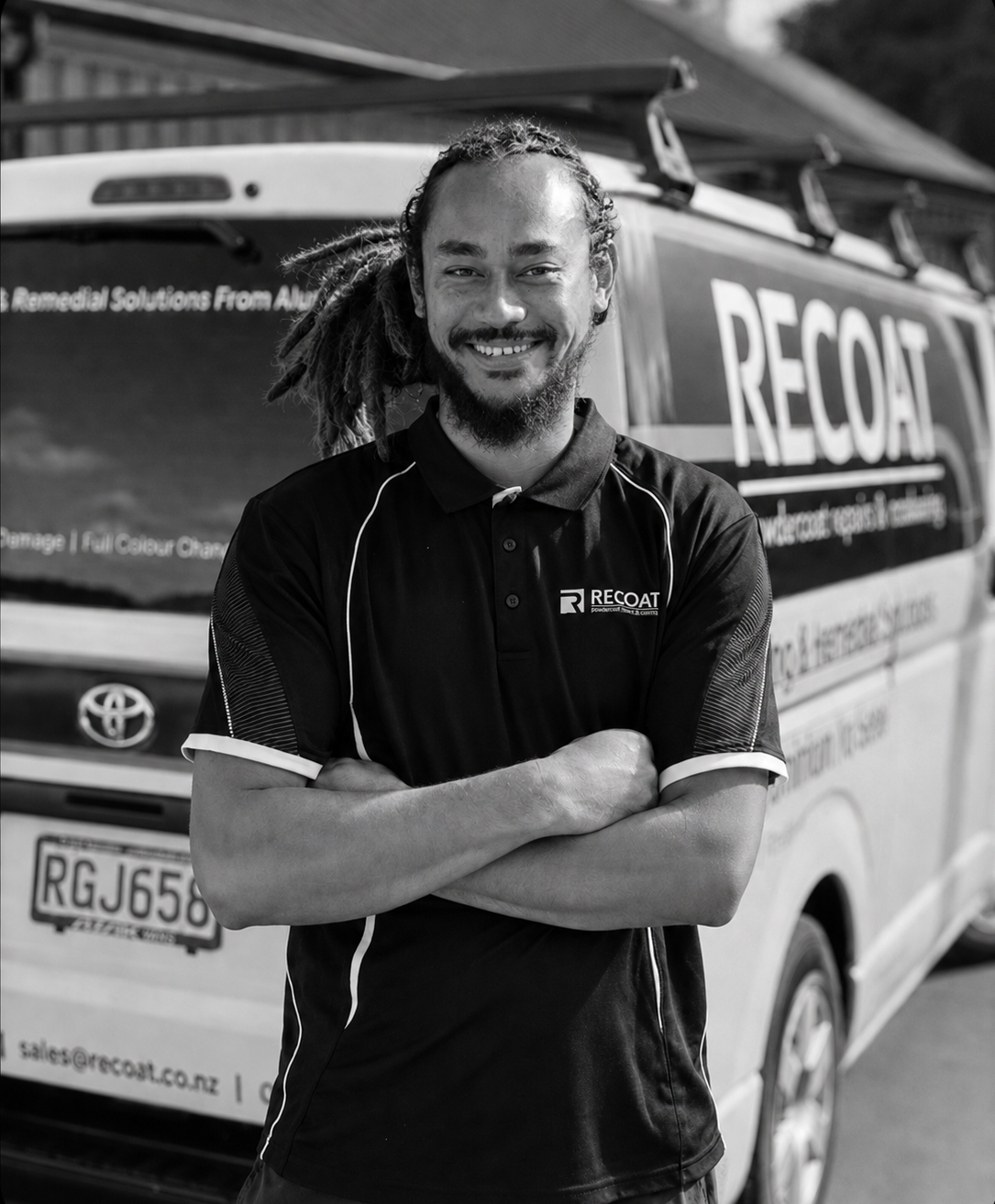 Smiling man with dreadlocks and beard in front of RECOAT service van, arms crossed, wearing a black polo shirt with RECOAT logo.