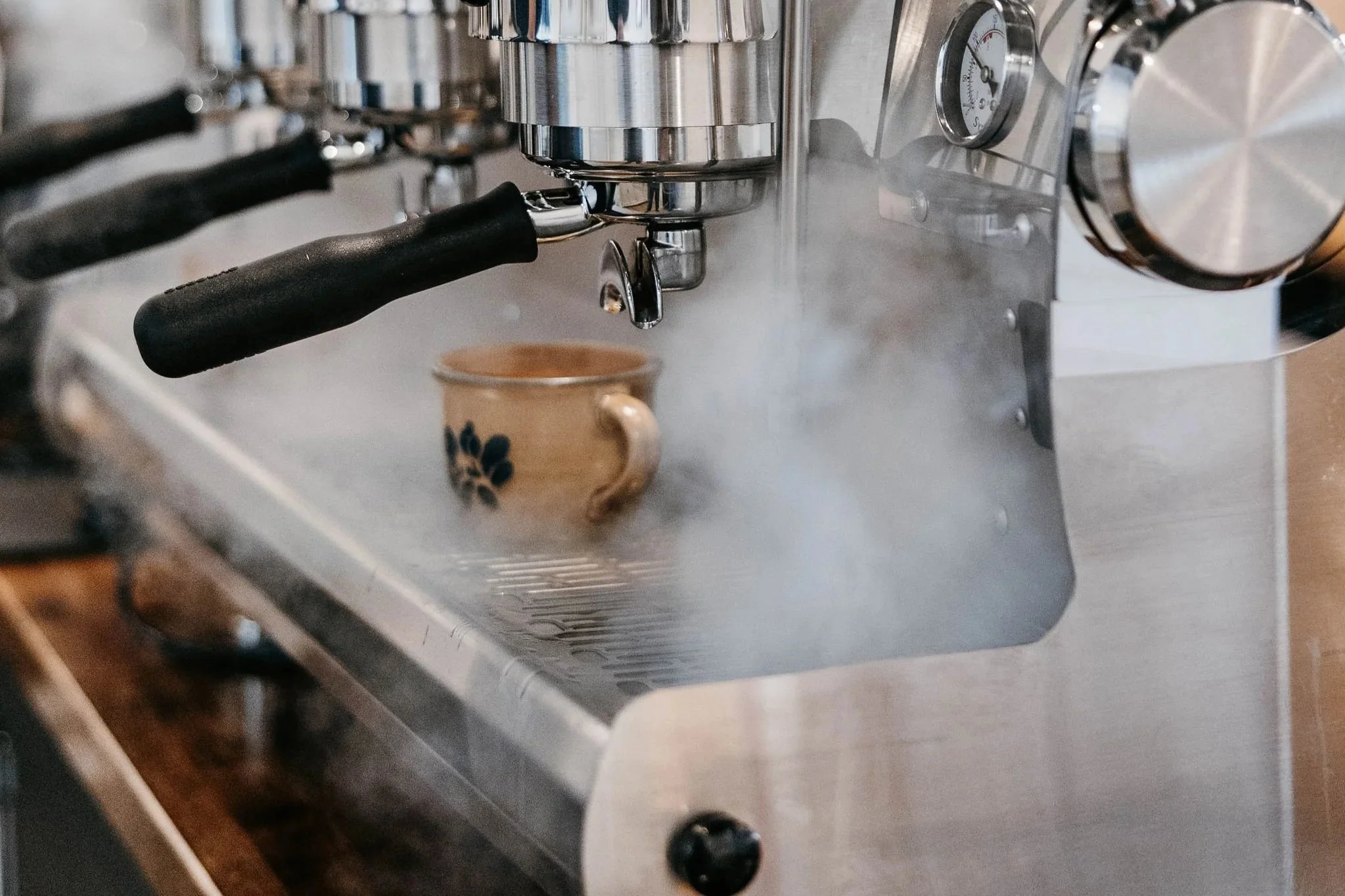 An espresso machine brewing coffee into a patterned ceramic mug with steam rising from it.