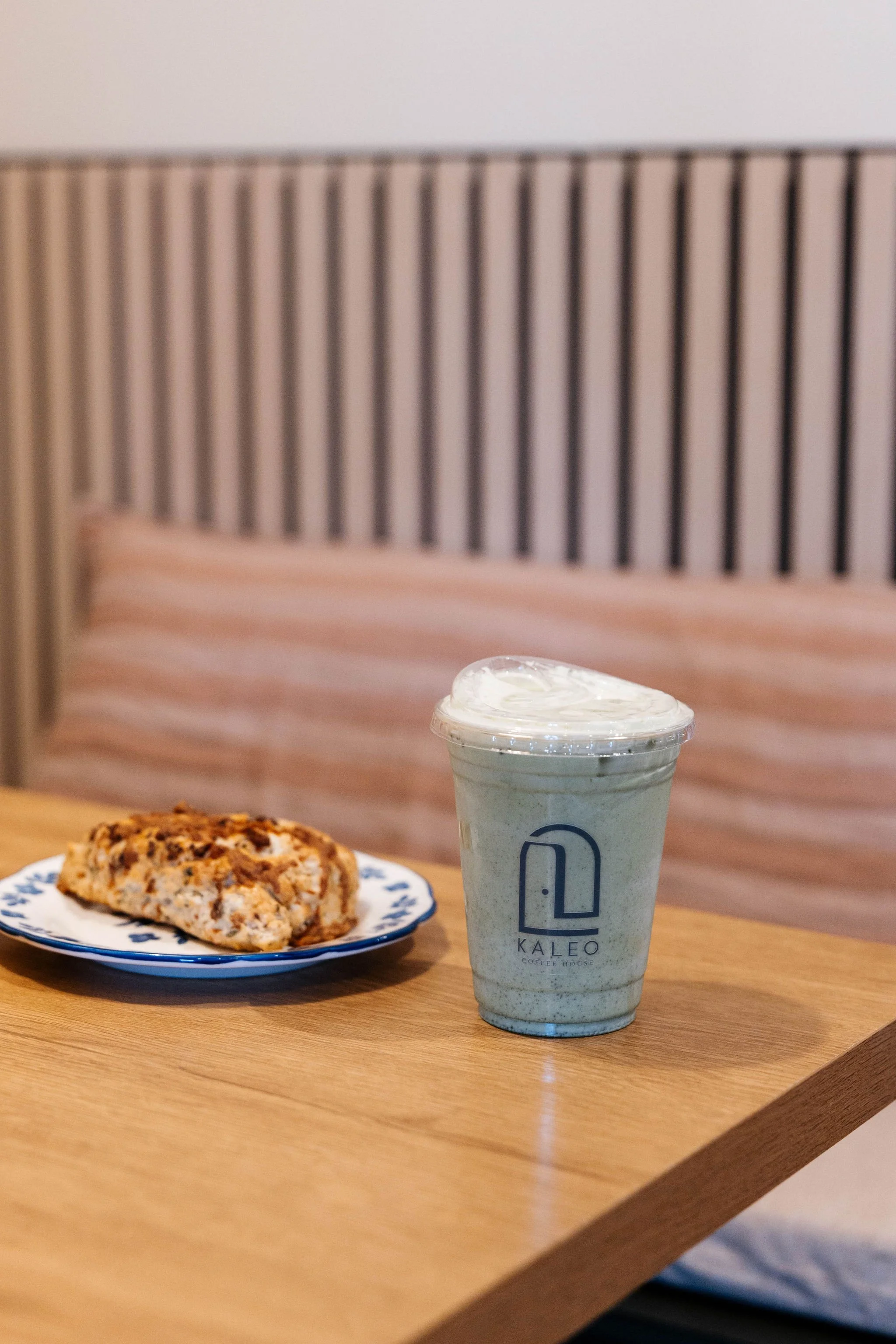 A plate with a sliced cookie and a drink from Kaleo Coffee House on a wooden table in a cafe.
