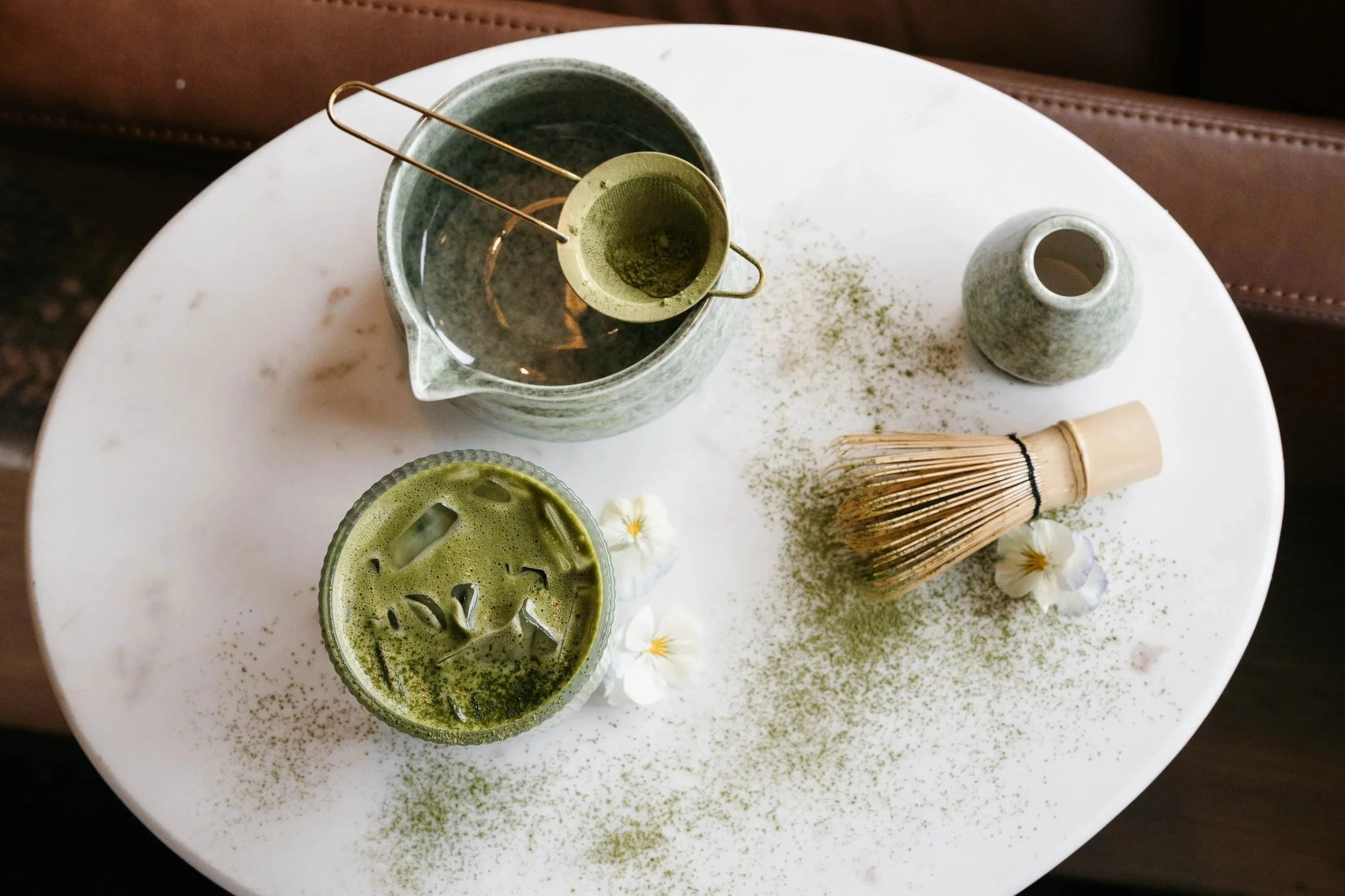 A hand holding a large plastic cup with a clear lid, containing a green blended drink from Kaleo Coffee House.