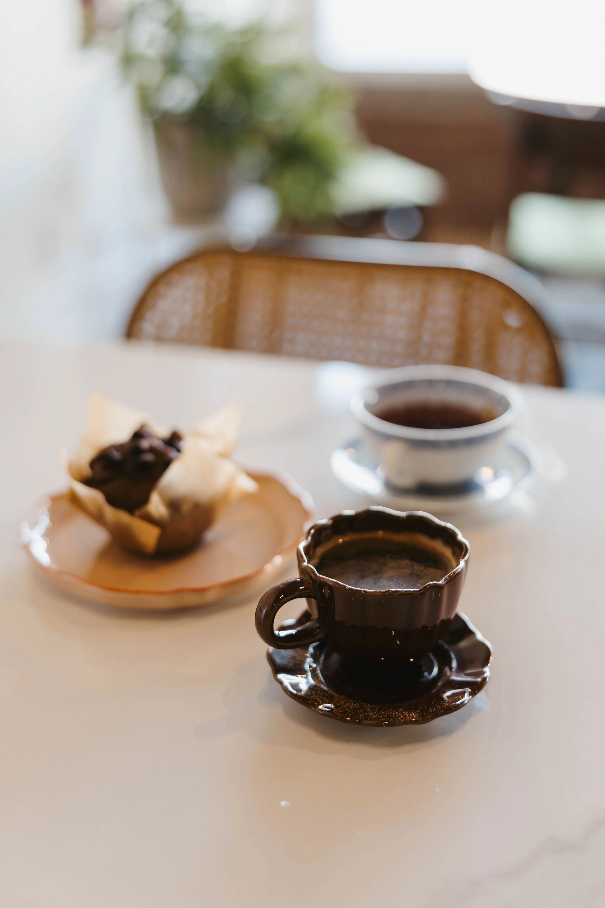 Two cups of coffee and a muffin on a table in a cozy cafe setting.