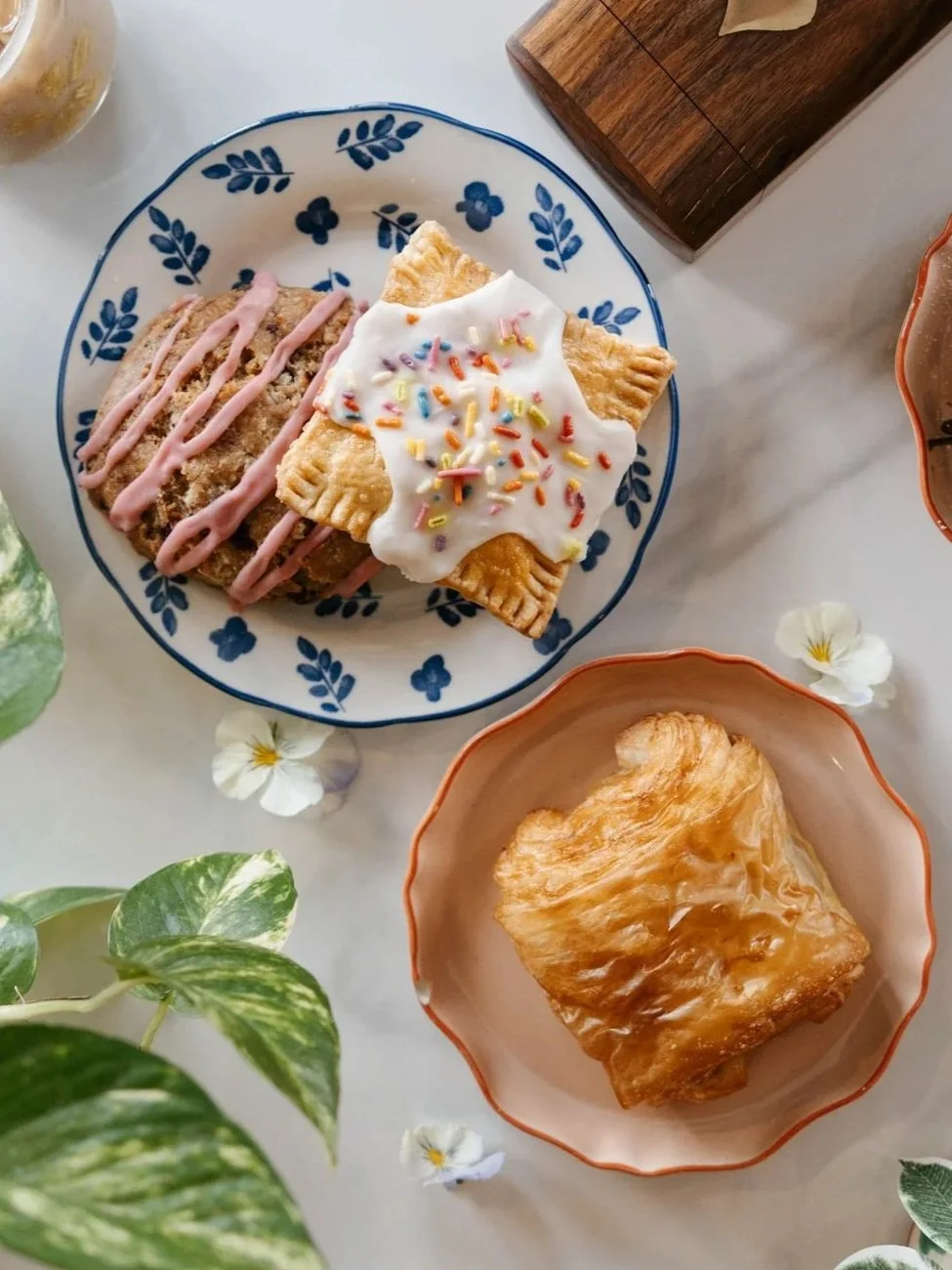 A blueberry muffin on a white plate with blue floral patterns, with a dark coffee mug in the background.