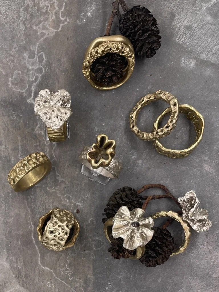 Assortment of gold and silver rings with textured and floral designs, some with attached dark brown or black drawstring accessories