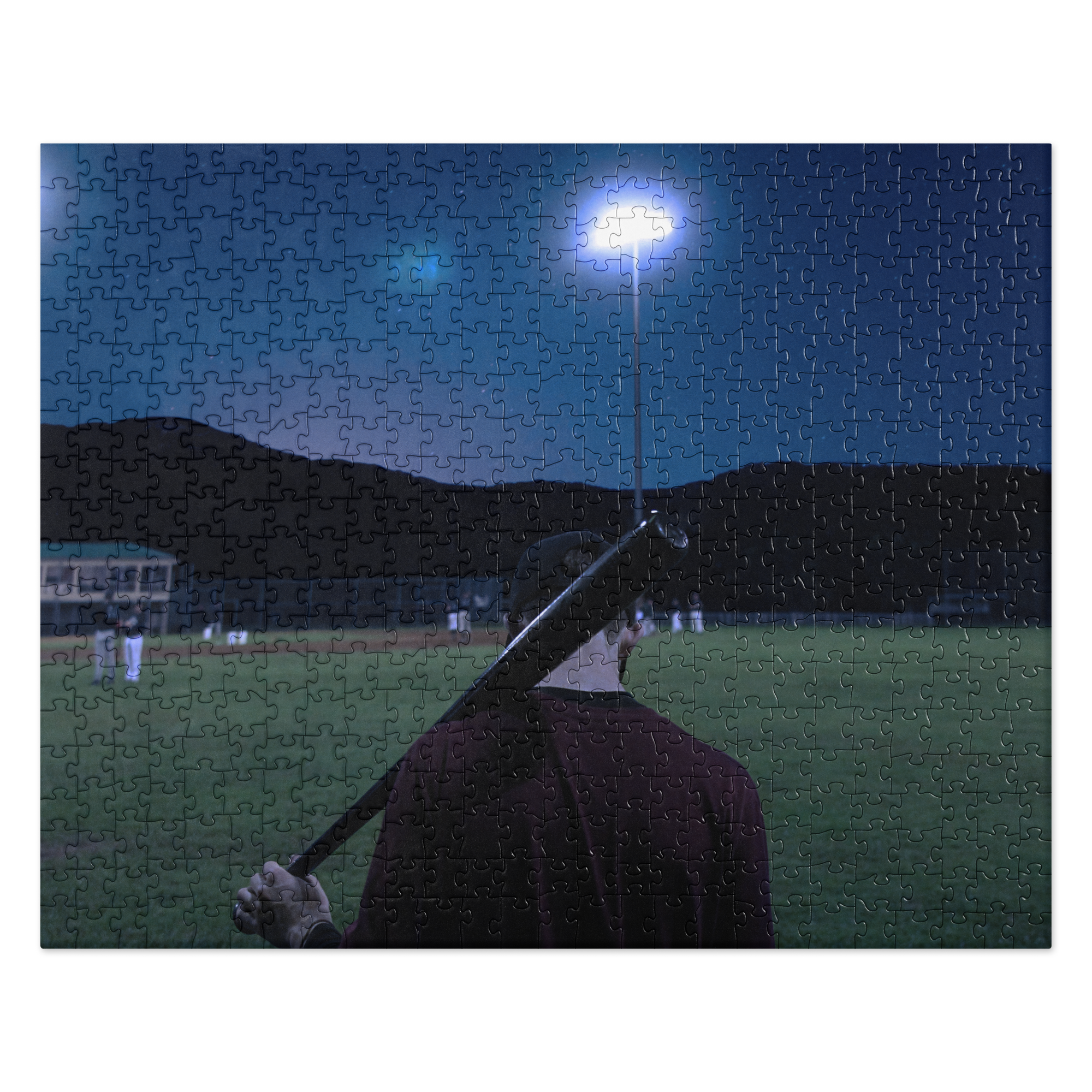 Puzzle - Moonshot - Completed jigsaw puzzle. Artwork depicts a person standing on a grass field holding a bat over their shoulder, illuminated by a bright stadium floodlight against a dark sky.