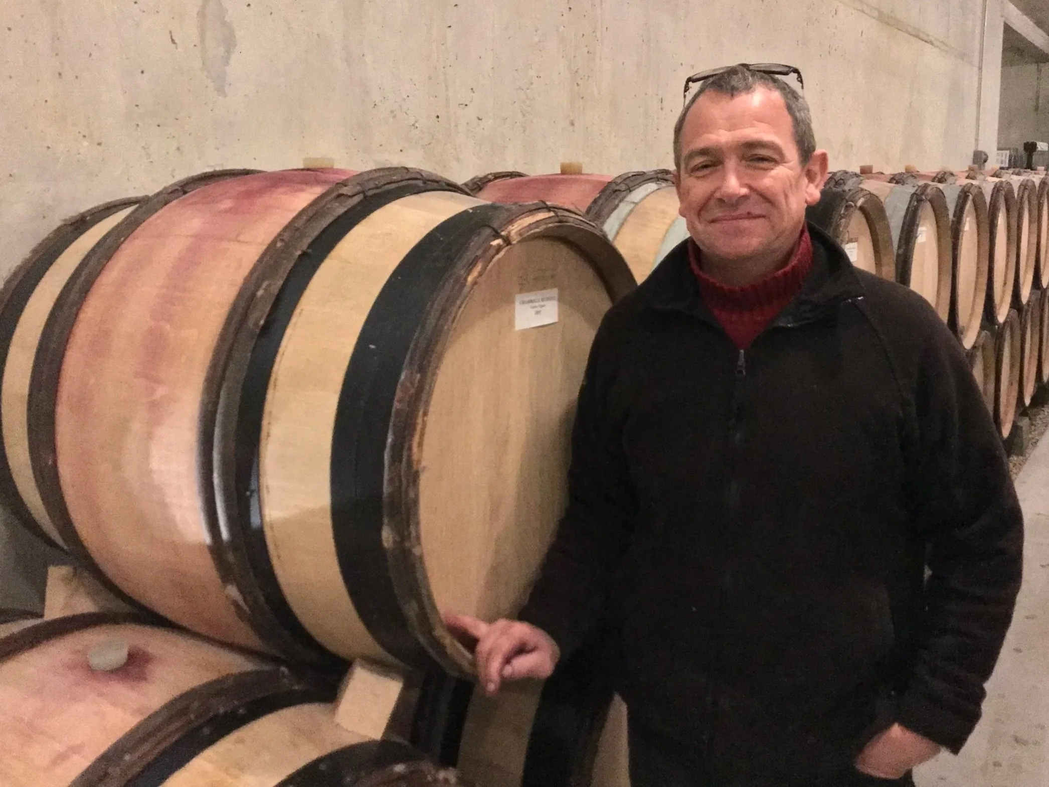 Dominique Le Guen of Domaine Hudelot-Baillet standing beside stacked wine barrels in the winery cellar.