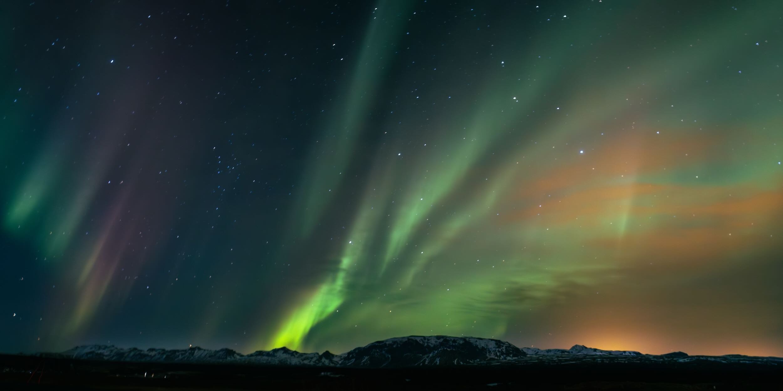 Northern lights across a night sky with stars and mountain silhouette.