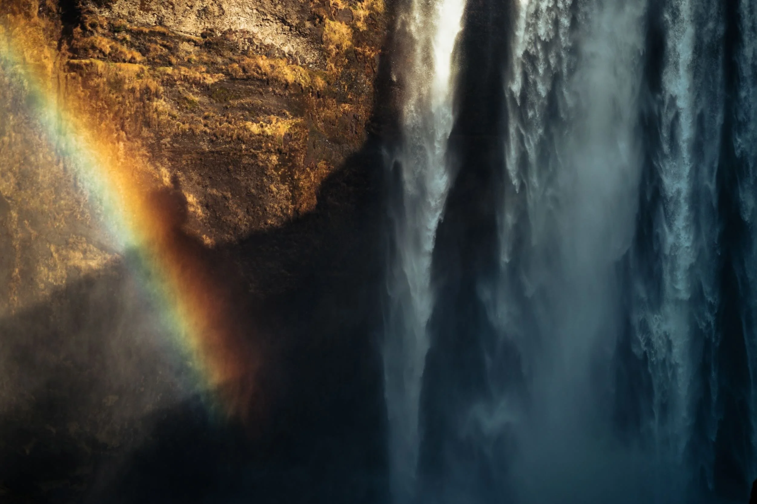 A waterfall cascading down a rocky cliffside with a rainbow visible on the left side of the image.