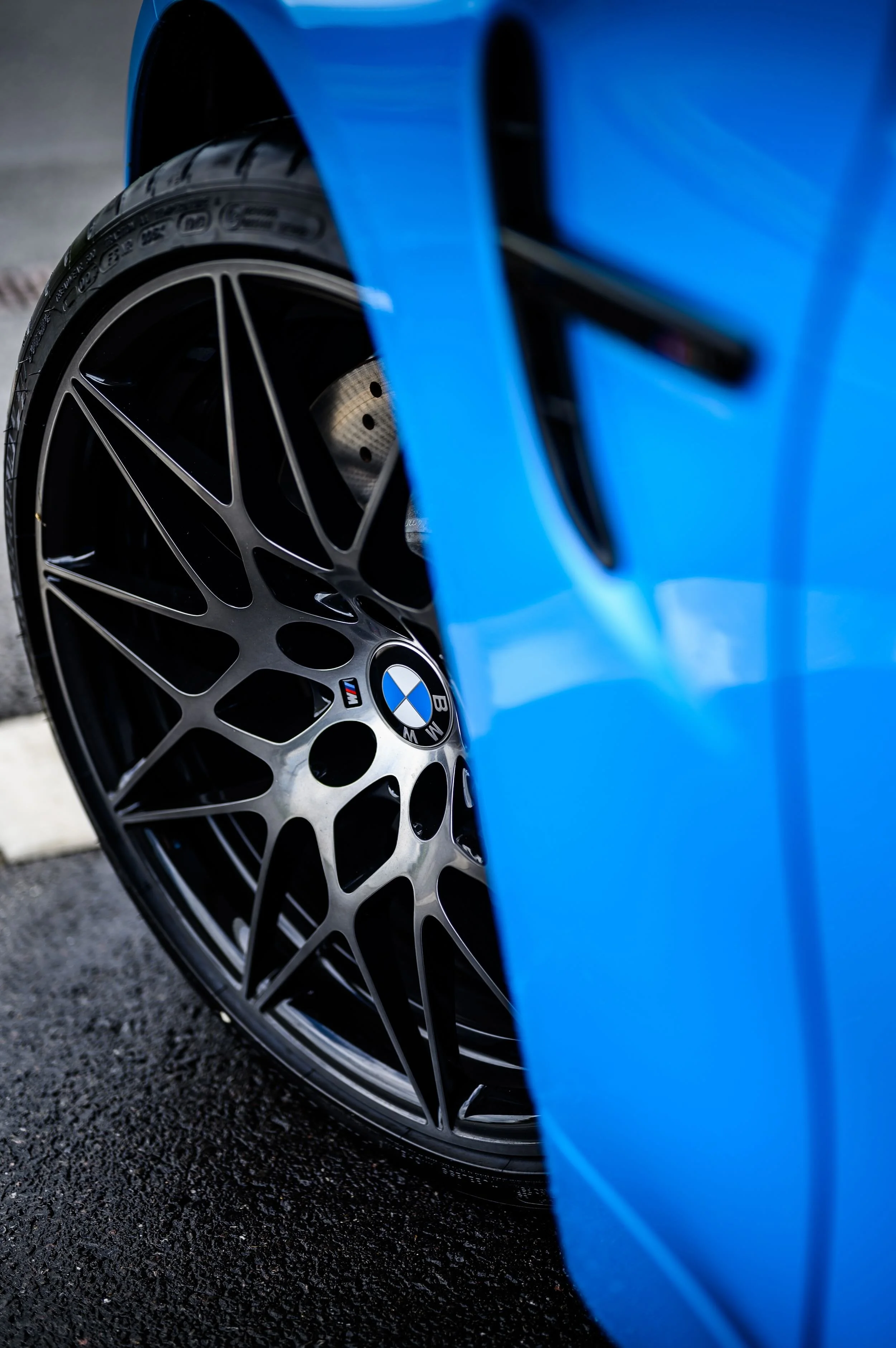 Close-up of a blue car's front wheel and tire, featuring the BMW logo, with a portion of the car's body visible.