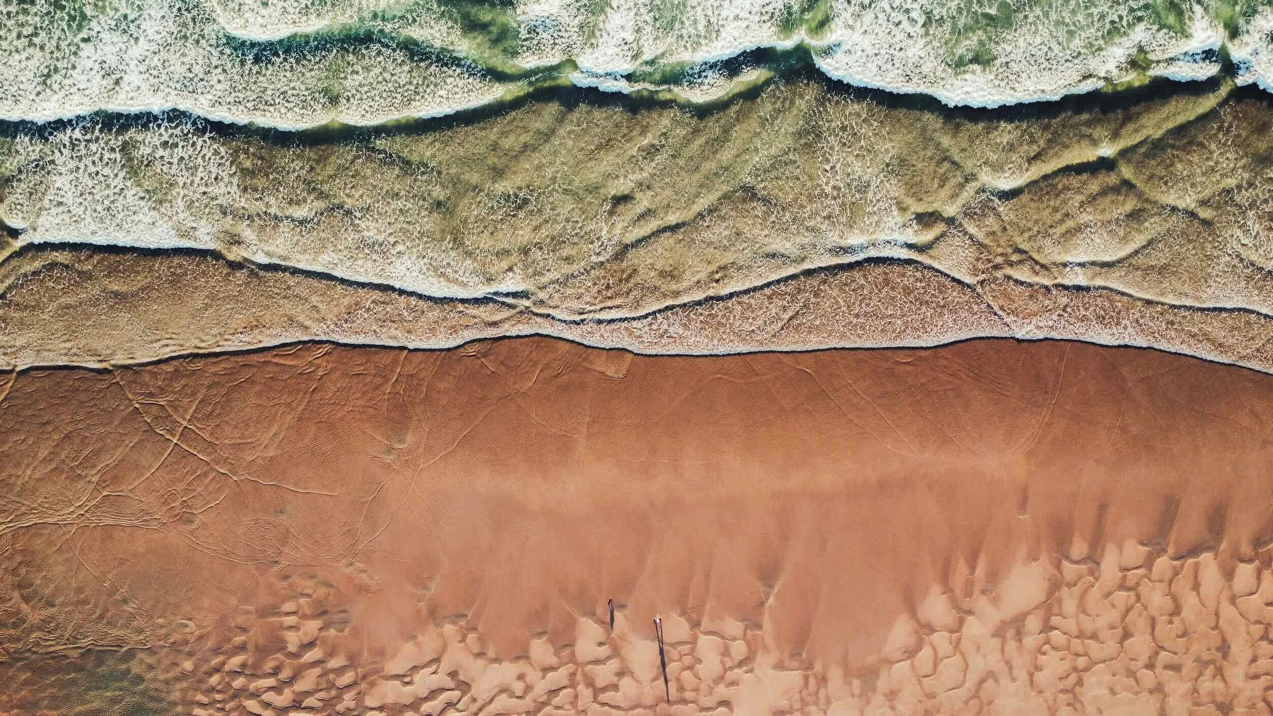 An aerial view of a beach with waves crashing onto sand dunes.