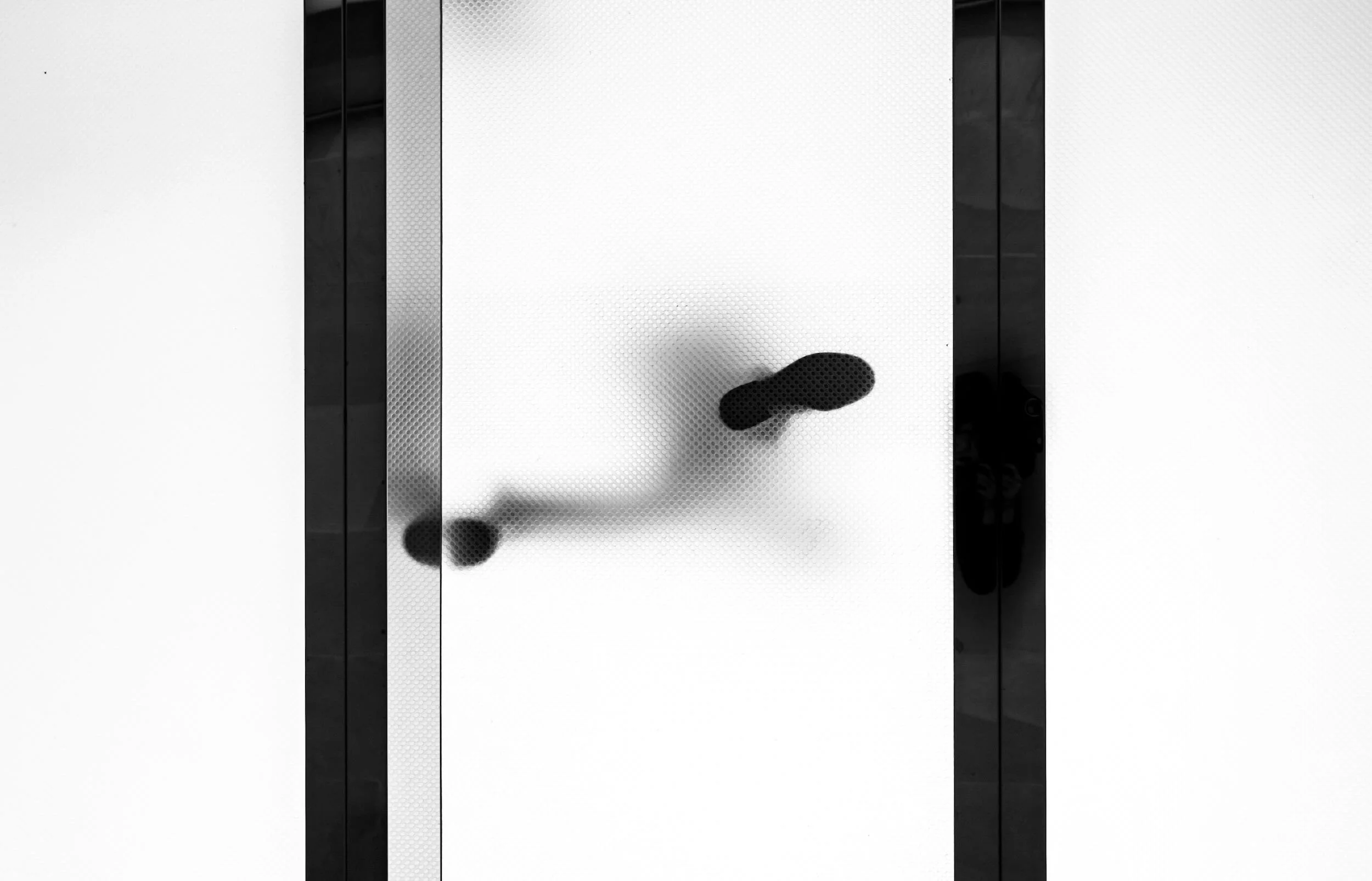 Close-up of an elevator interior door with a black, abstract shape on the frosted glass surface, black door frames on either side.