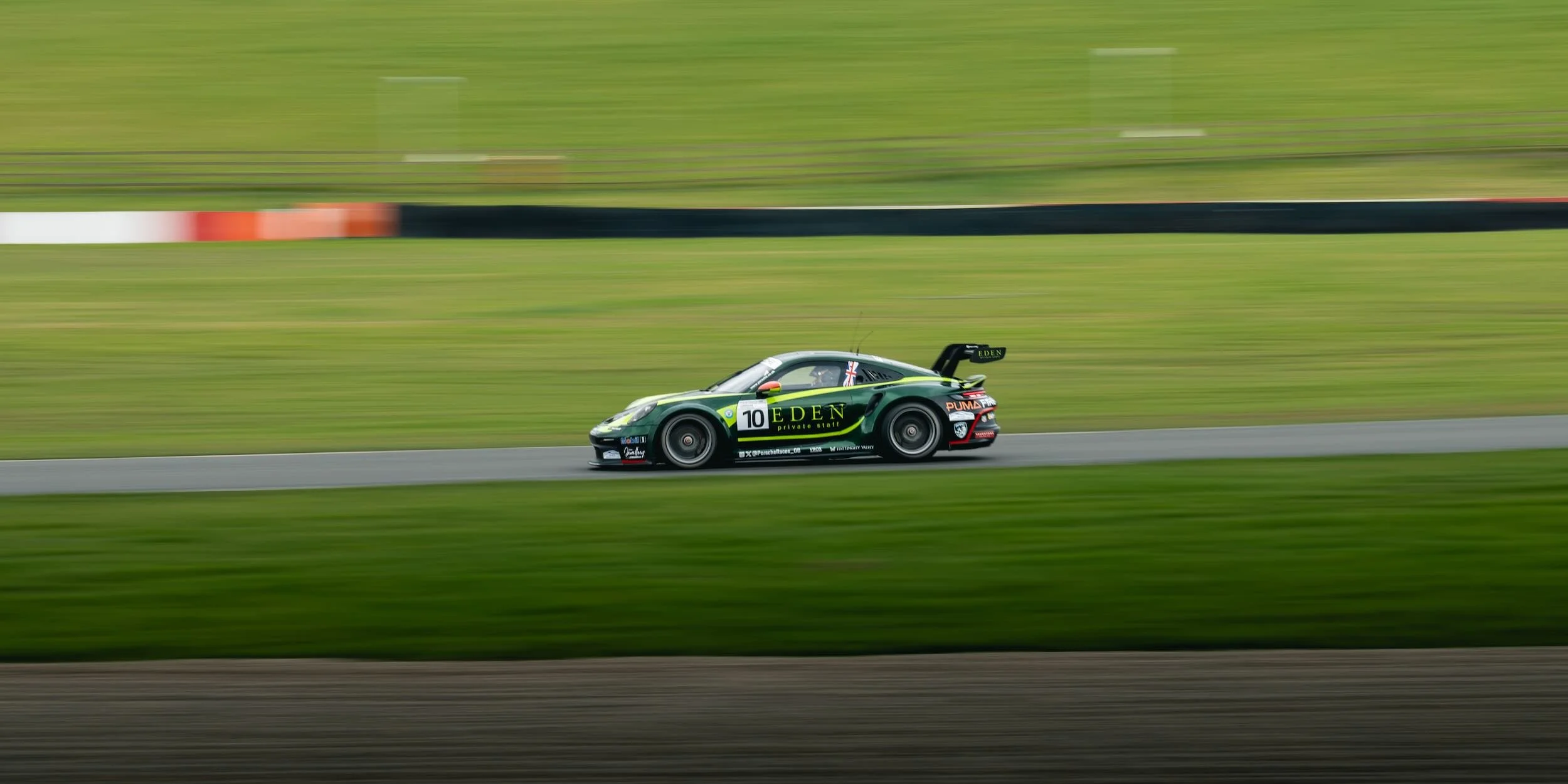 A race car speeding along a racetrack with blurred green grass and safety barriers in the background, featuring sponsorships and the number 10.