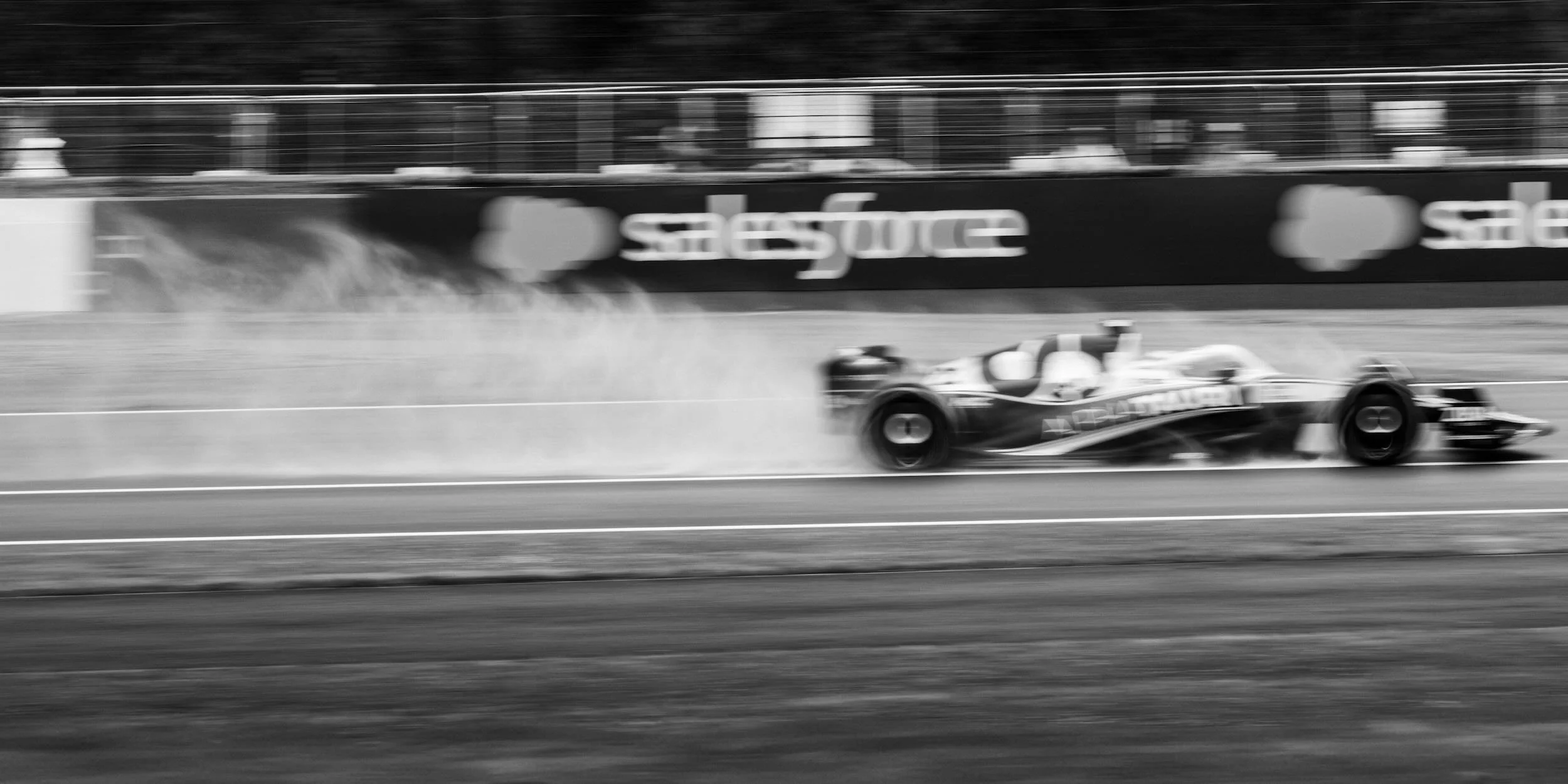 Black and white photo of a race car moving at high speed on a race track, with blurred background and tire smoke.