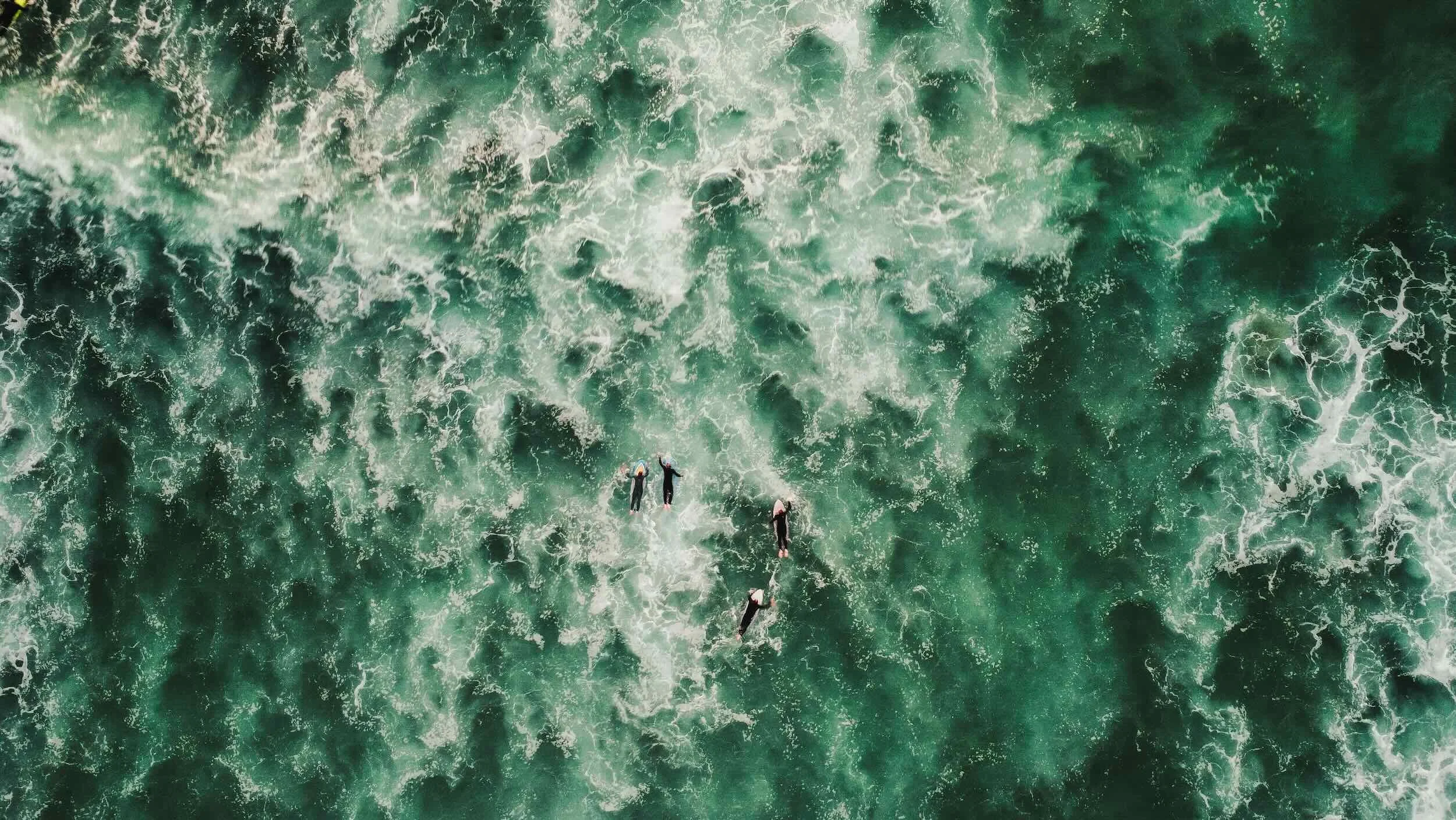 An aerial view of the ocean with four surfers riding a wave.