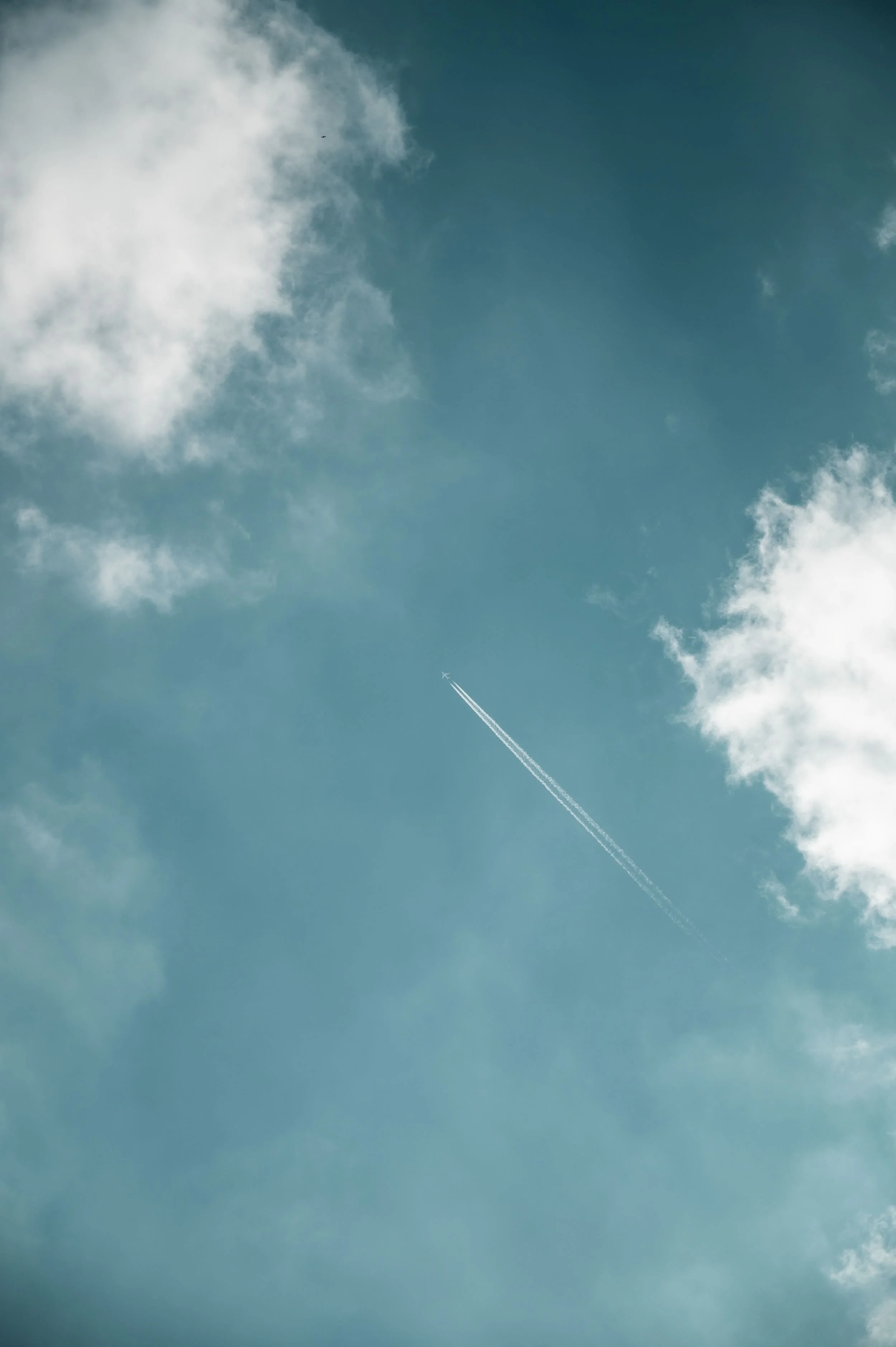 A clear blue sky with scattered clouds and a jet trail.