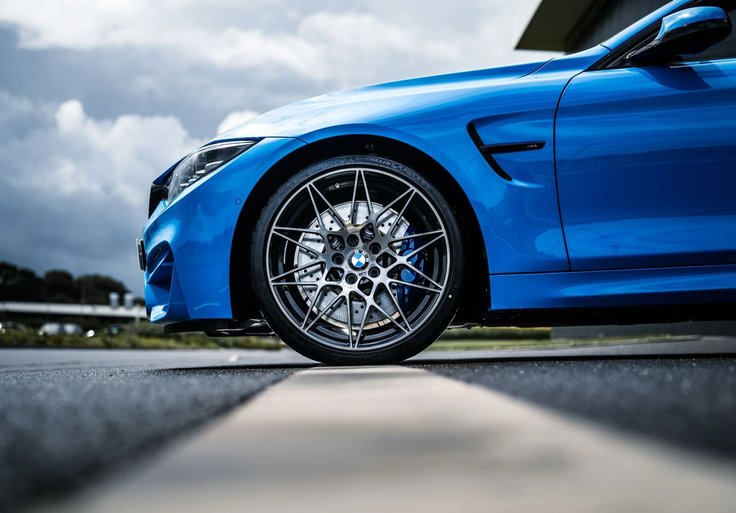 Close-up view of the front wheel of a blue BMW sports car, showing the intricate wheel design and tire, under cloudy sky.