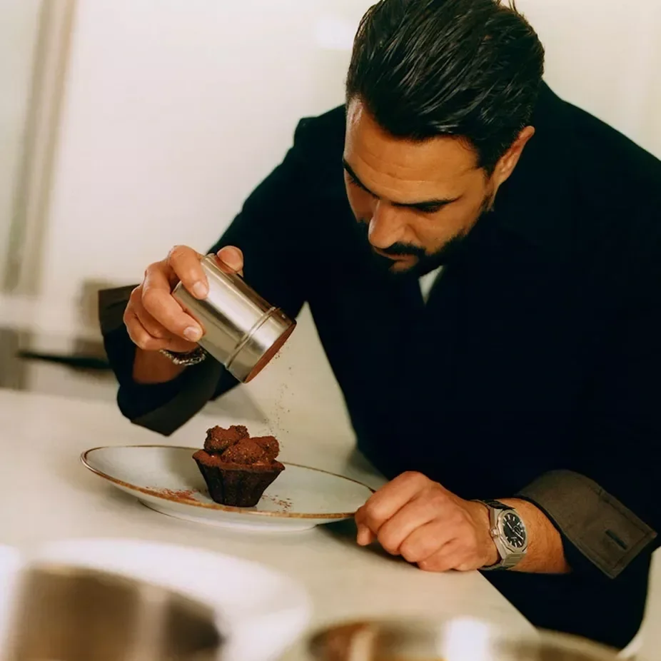 Le chef Jeffrey Cagnes en cuisine saupoudrant un dessert, portant la pièce vestimentaire lifestyle co-brandée créée avec Figaret.