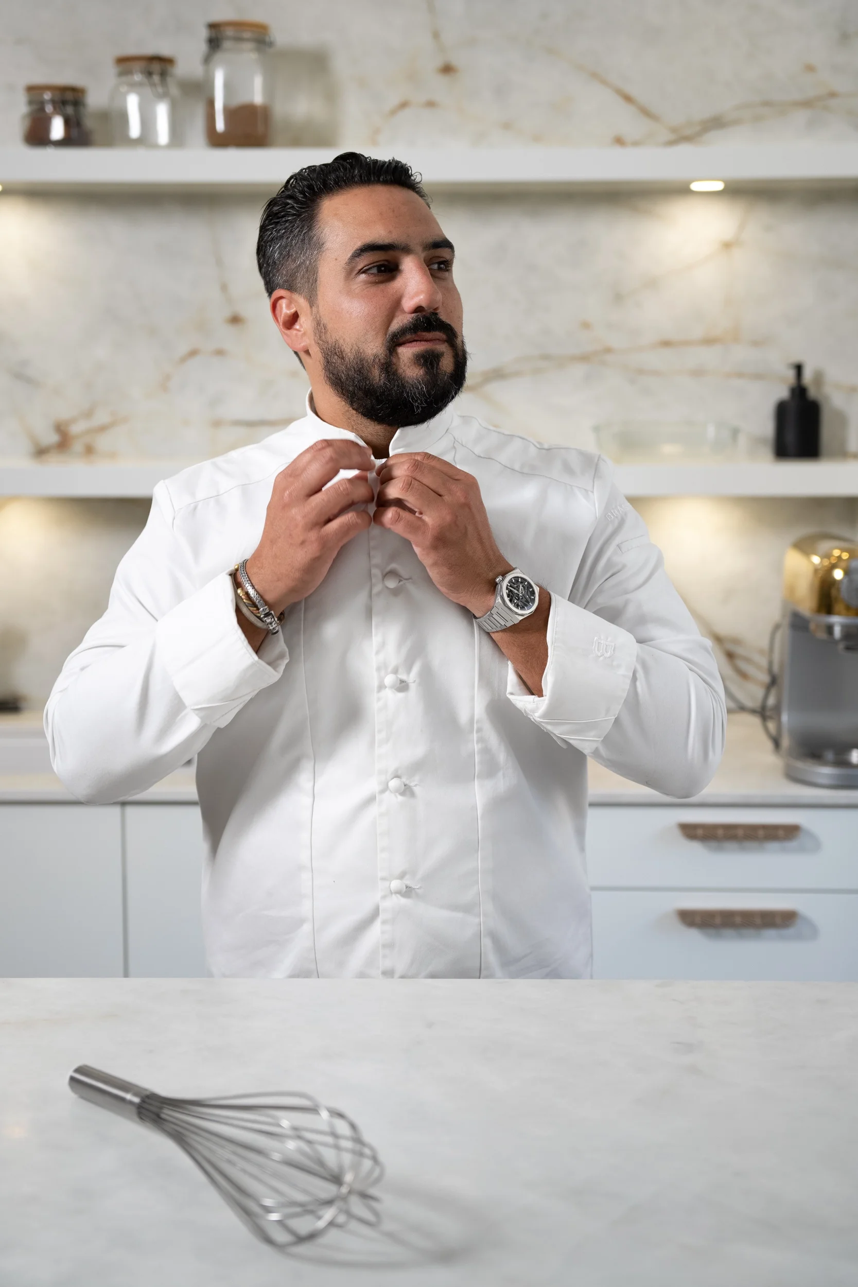Portrait du Chef pâtissier Jeffrey Cagnes ajustant sa veste blanche dans un laboratoire, illustrant l'incarnation de marque et la personnification de l'artisan dans le secteur F&B.