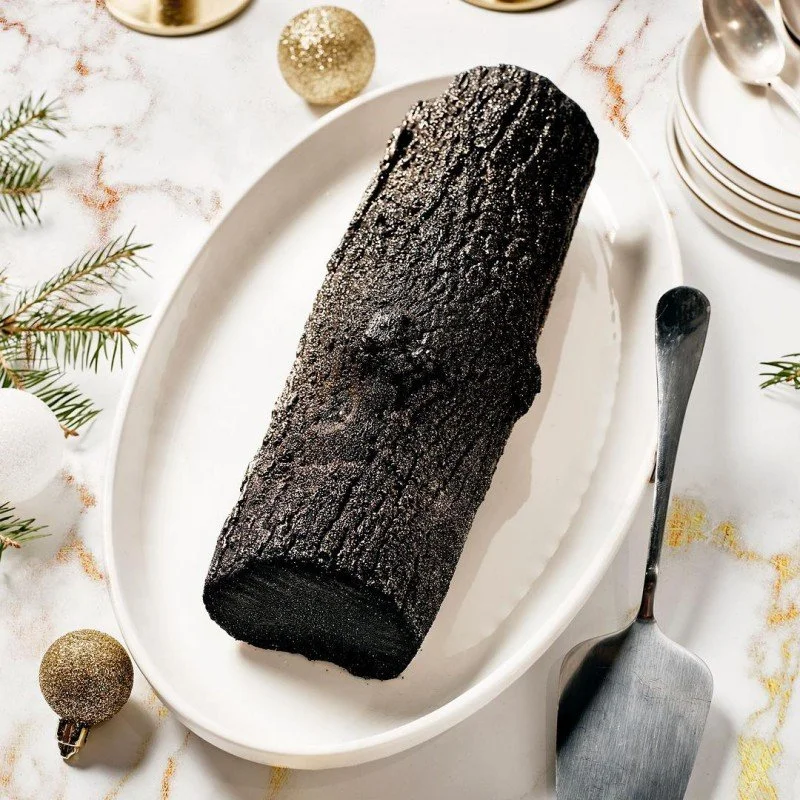 Bûche de Noël en forme de tronc d'arbre noir texturé sur un plat, réalisée avec le moule sur-mesure Silikomart pour Philippe Conticini.