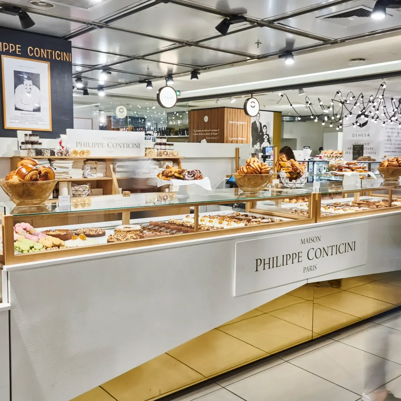Vue d'ensemble du corner de la Maison Philippe Conticini aux Galeries Lafayette avec sa vitrine dorée et ses pâtisseries haut de gamme.