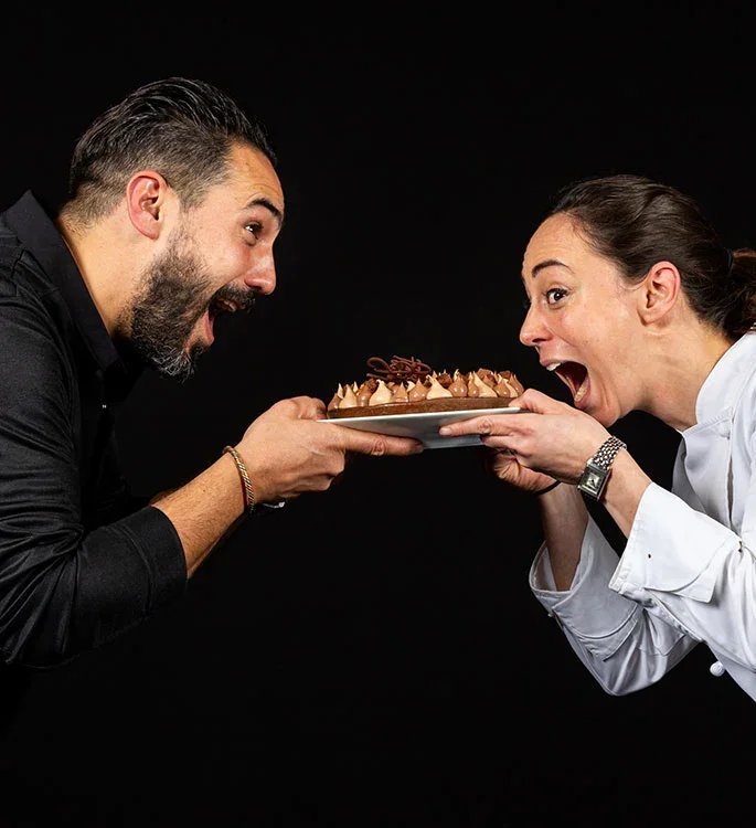 Les chefs pâtissiers Jeffrey Cagnes et Nina Métayer s'amusant face à face en tenant une tarte au chocolat lors du Salon du Chocolat.