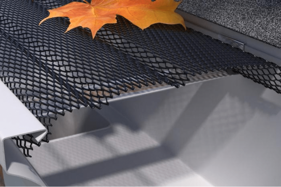 A black metal mesh table with a yellow autumn leaf resting on it, and part of a gray surface in the background.